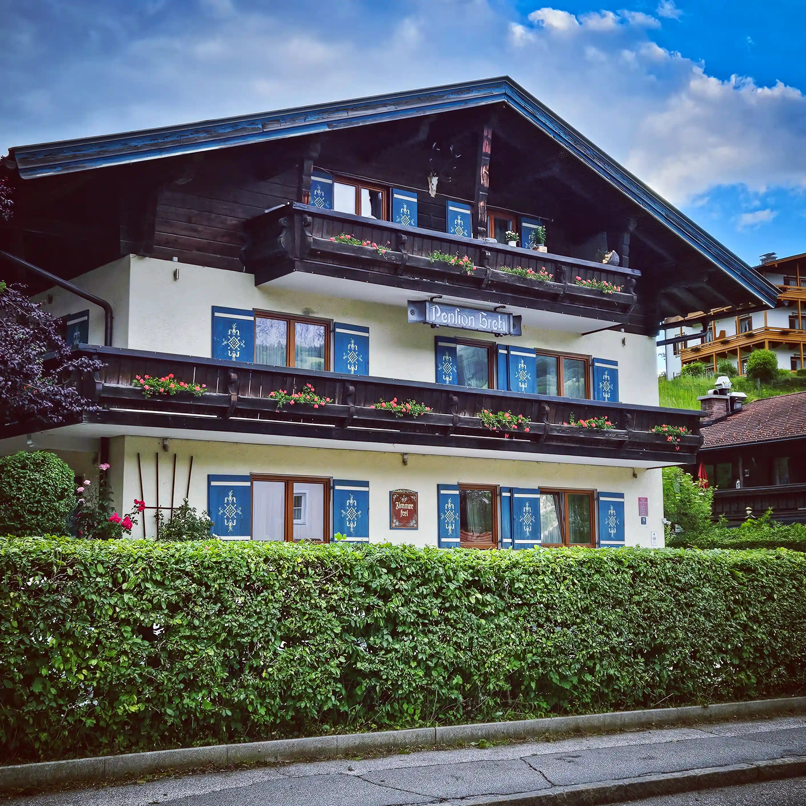 A traditional Alpine guesthouse with blue shutters, wooden balconies, flower boxes, and a sign reading “Pension Bichl.”