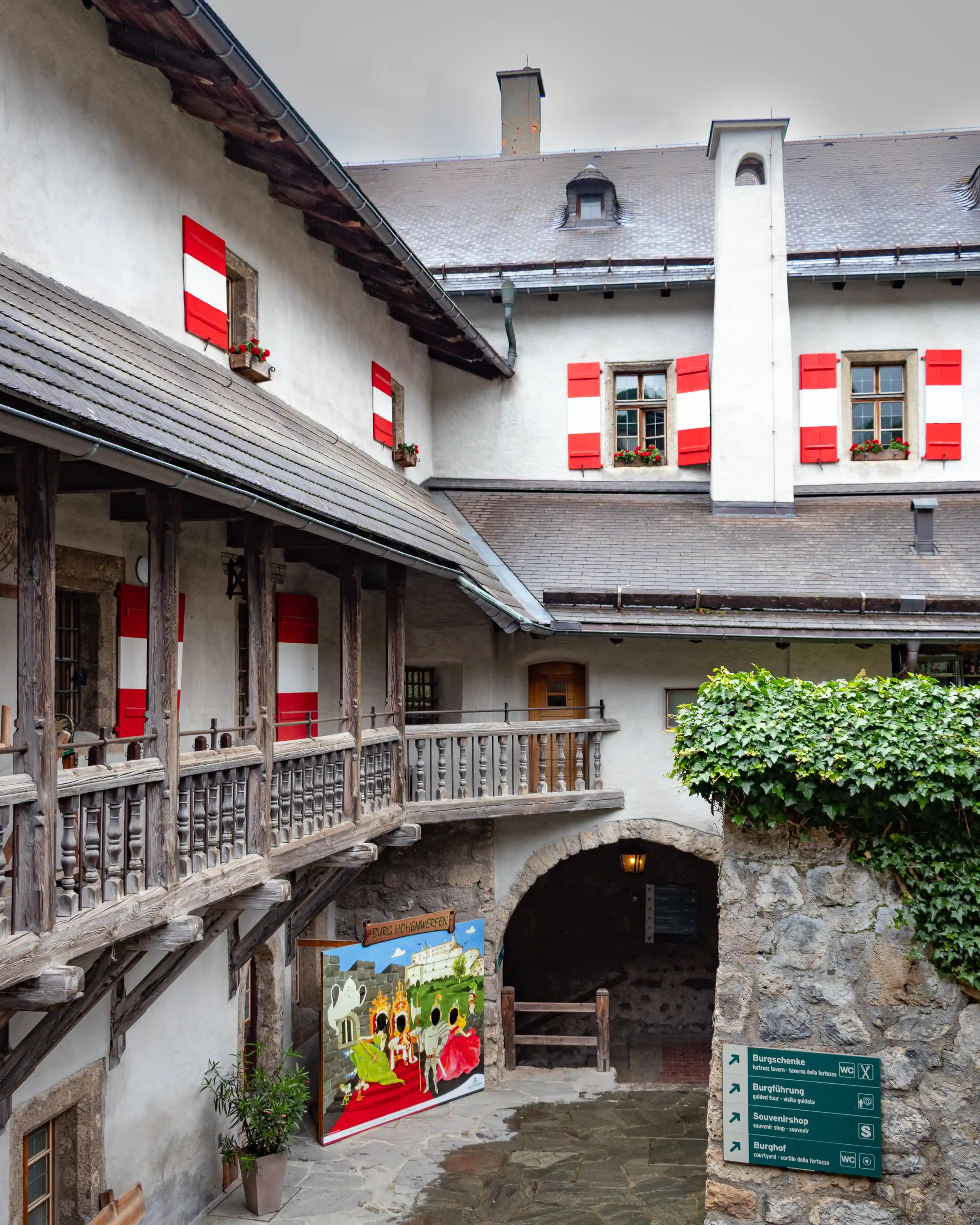 A stone courtyard inside Burg Hohenwerfen is lined with gray buildings, wooden balconies, and red-and-white shutters.