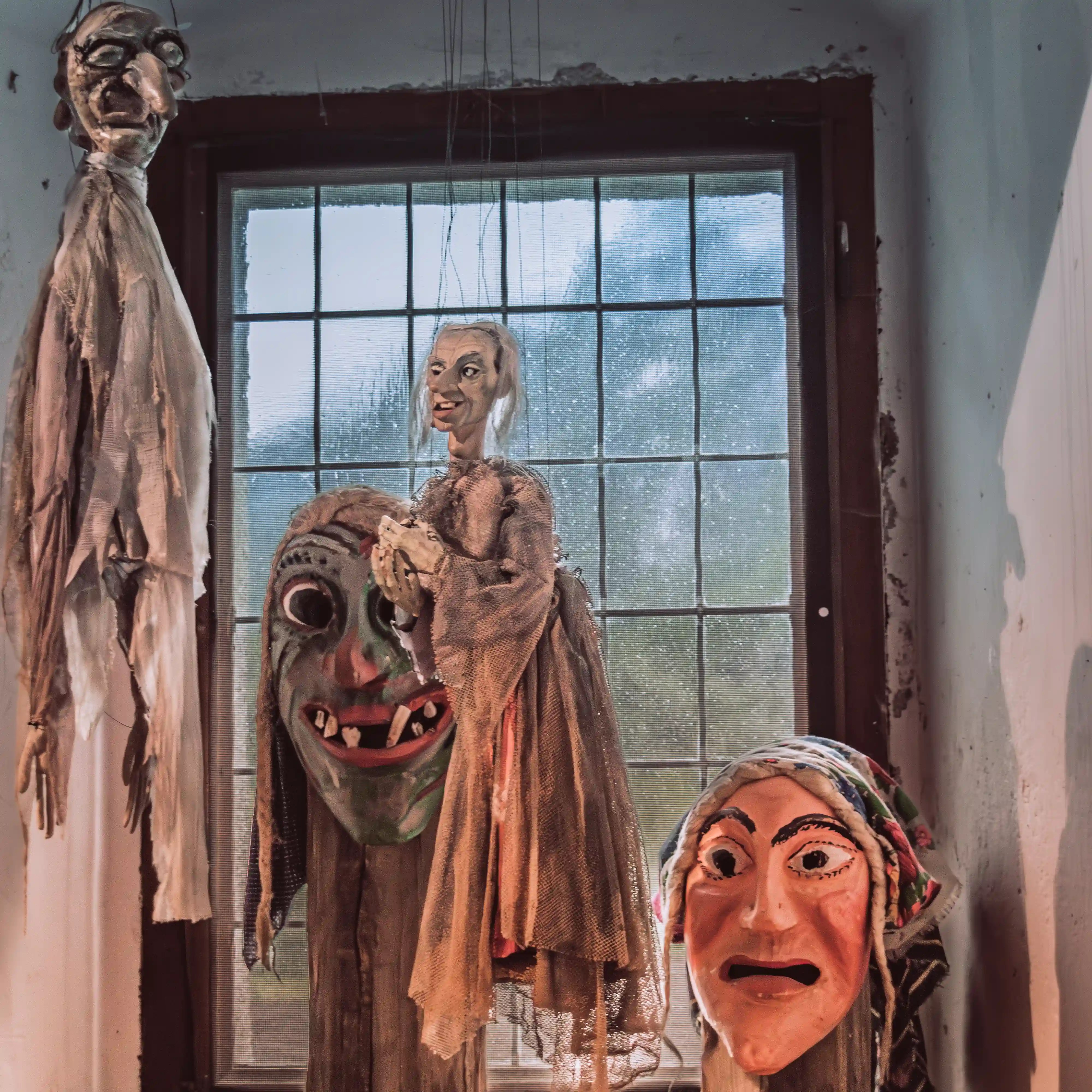 Wooden figures and masks hang near a window inside Burg Hohenwerfen, arranged as part of a dark historical display.