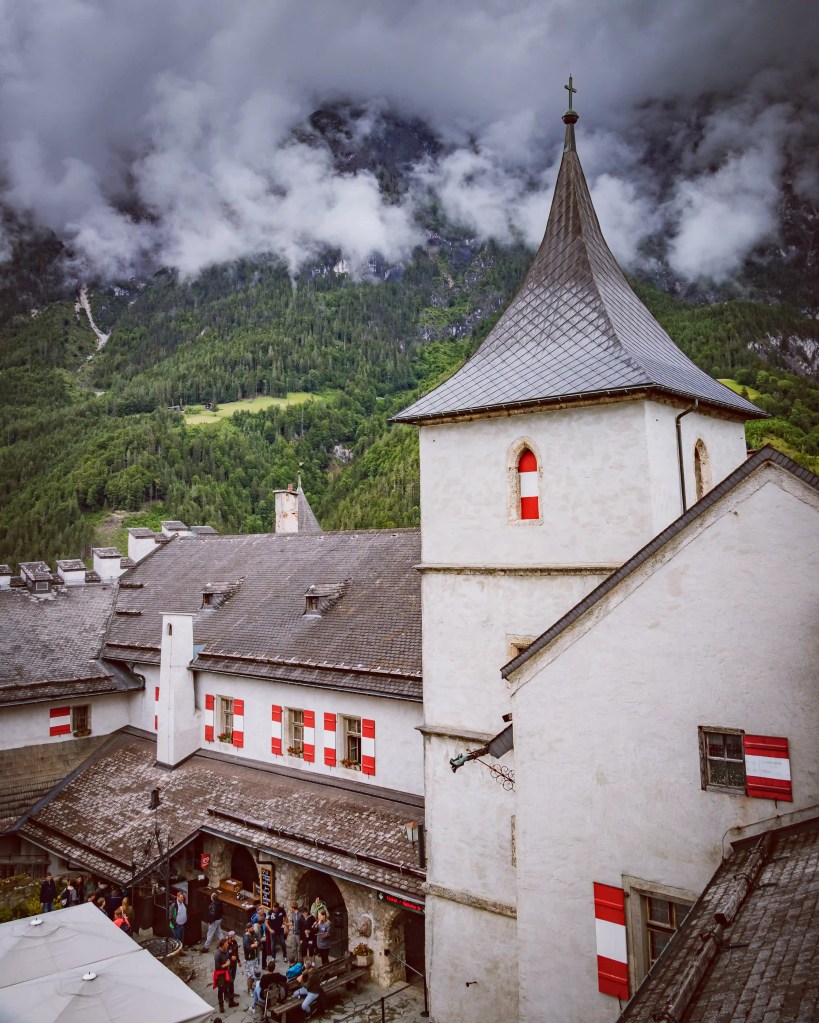A tall gray tower with red-and-white shutters rises above the courtyard buildings at Burg Hohenwerfen.
