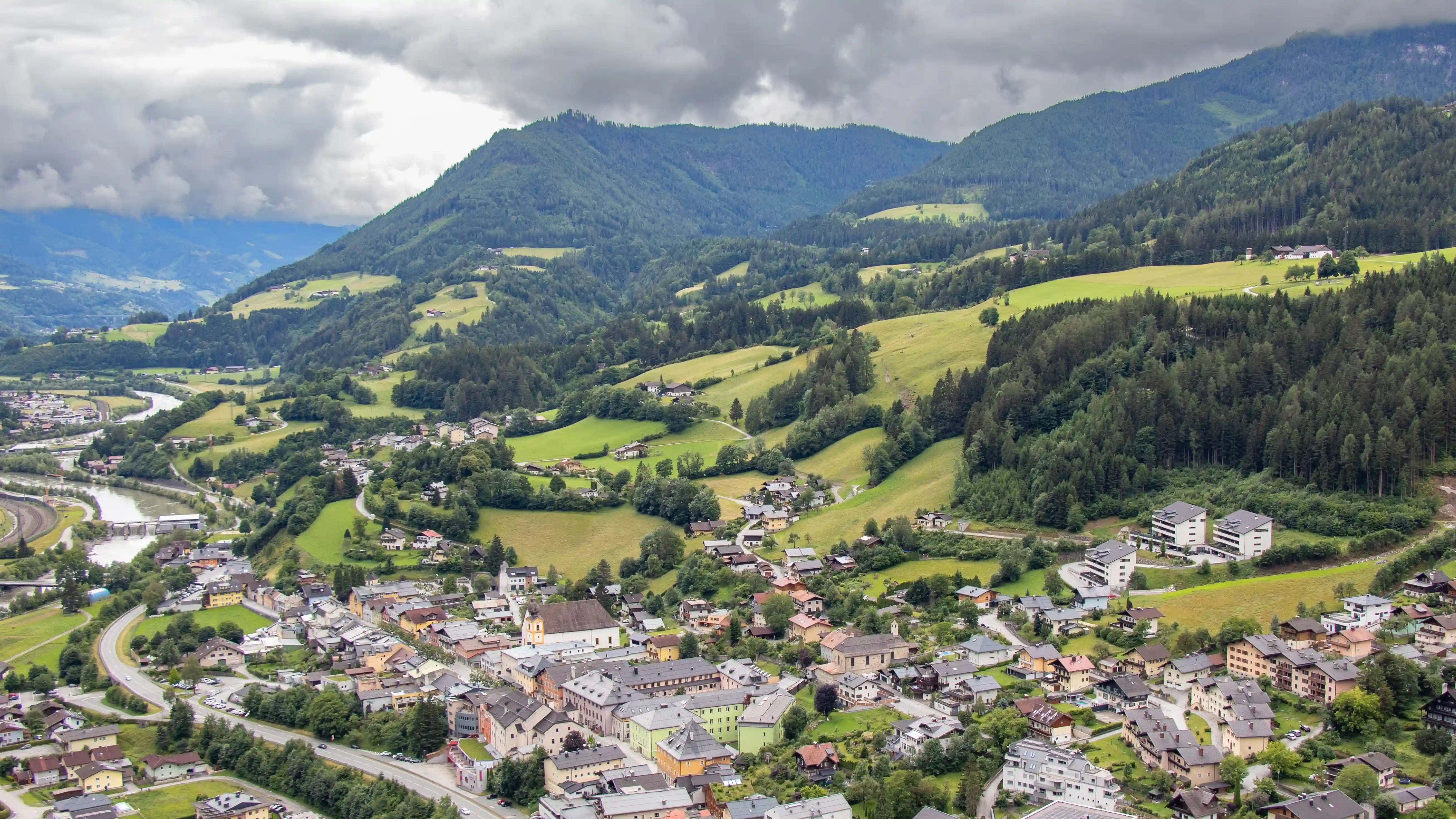 The town of Werfen spreads across rolling green hills with forests and scattered houses under a cloudy sky.