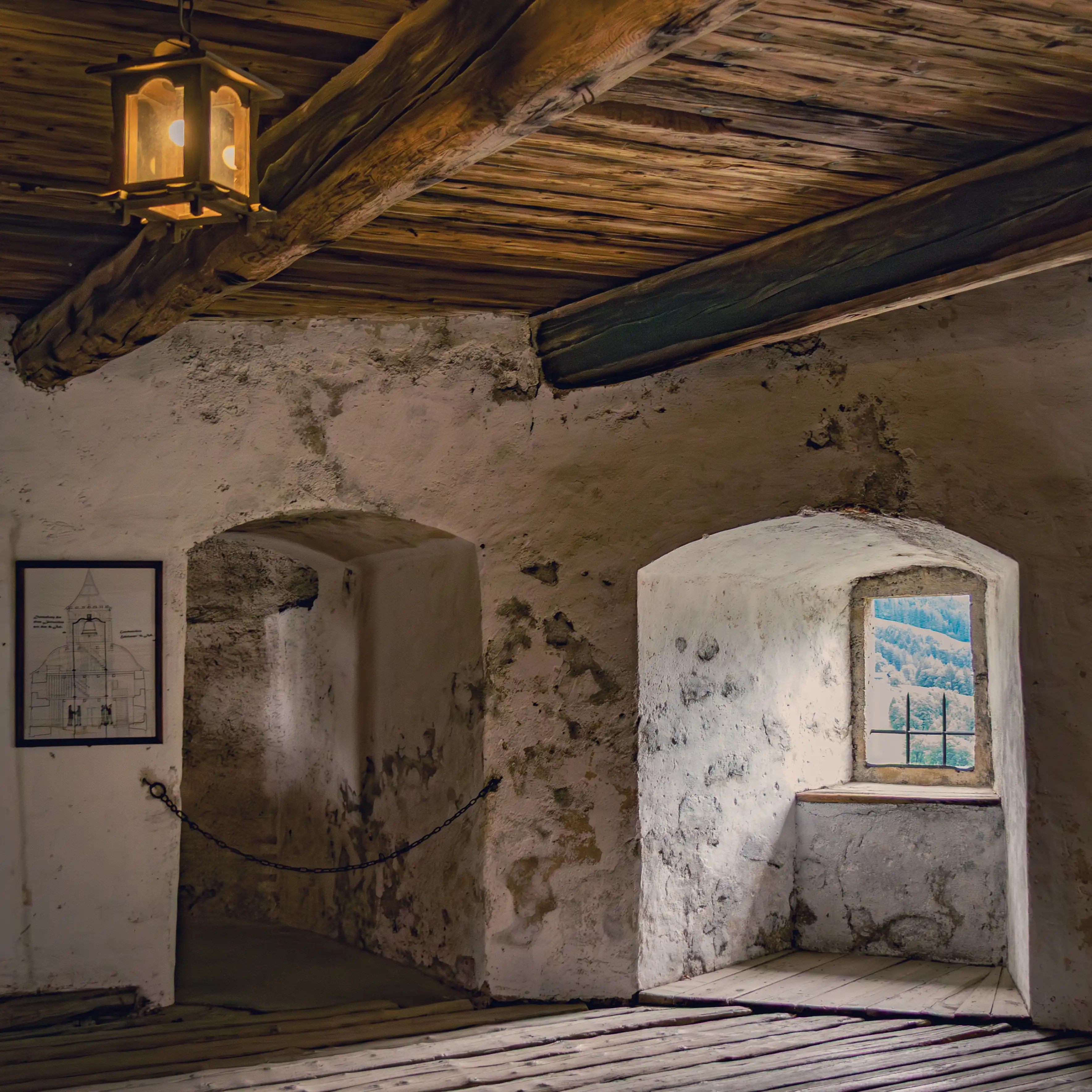 A stone interior room at Burg Hohenwerfen features small windows, thick walls, wooden beams, and a hanging lantern.