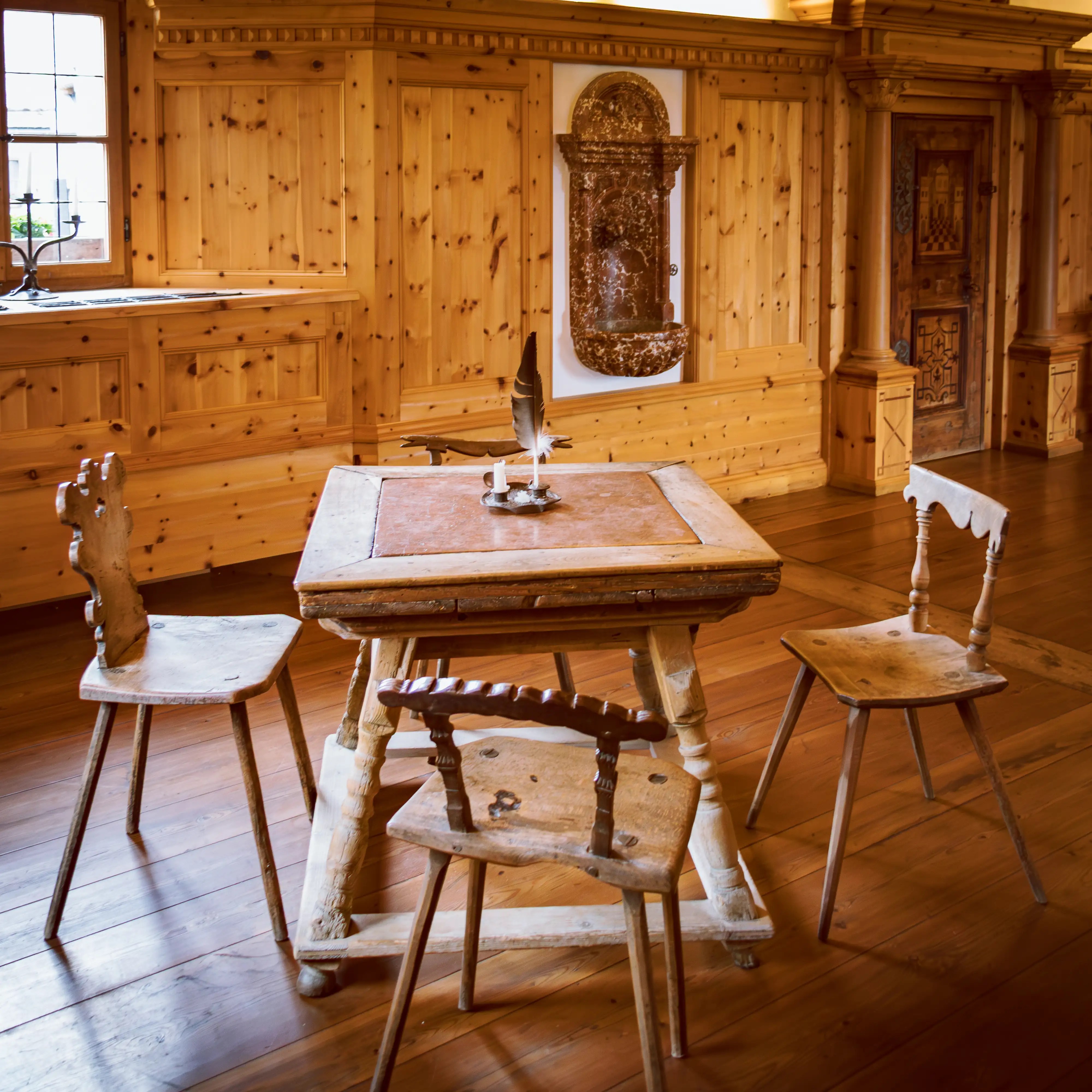A small wooden table with simple stools and a feather quill sits inside a wood-paneled historic room at Burg Hohenwerfen.