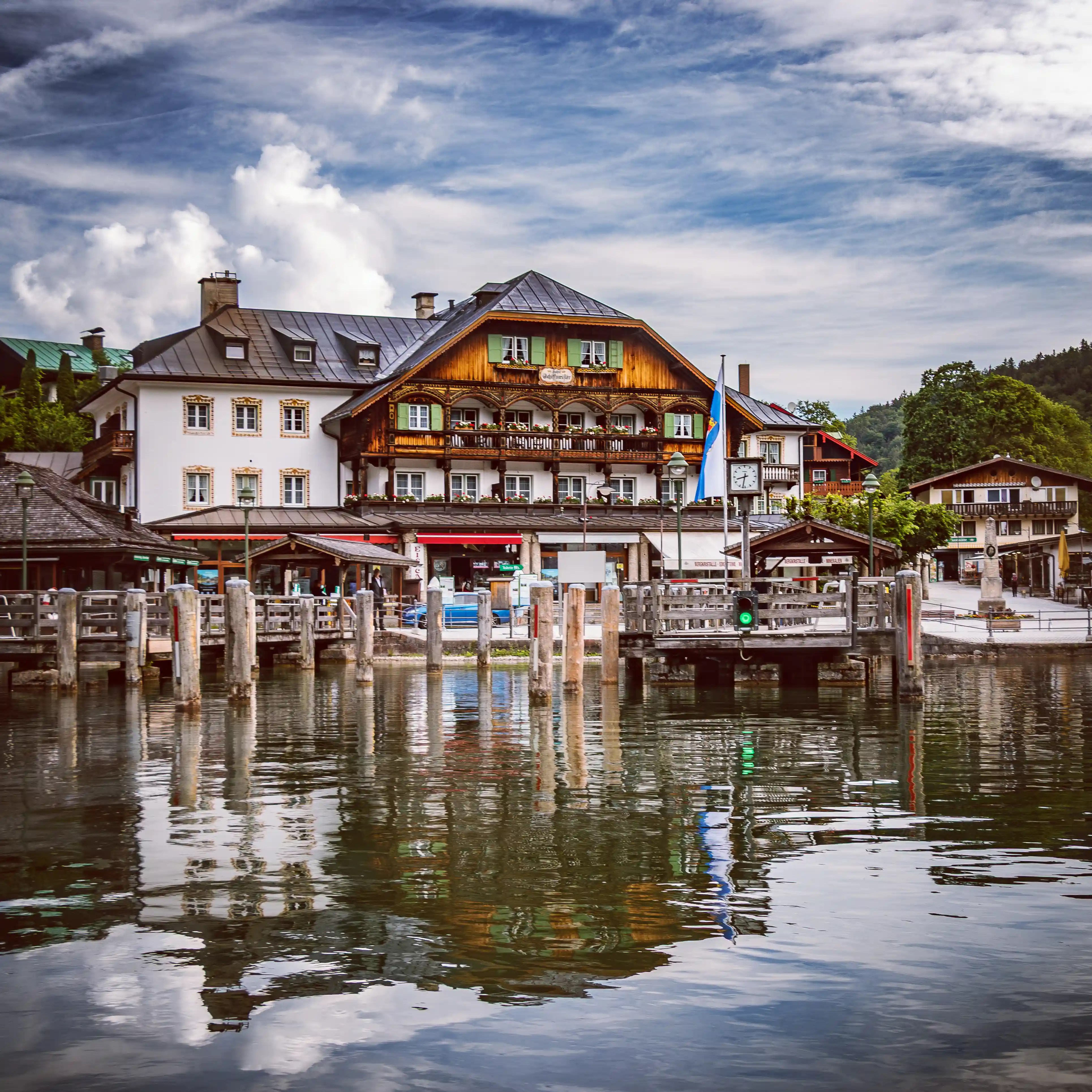 Traditional alpine buildings line the waterfront at Königssee, reflected in the calm lake with wooden boat piers in the foreground.