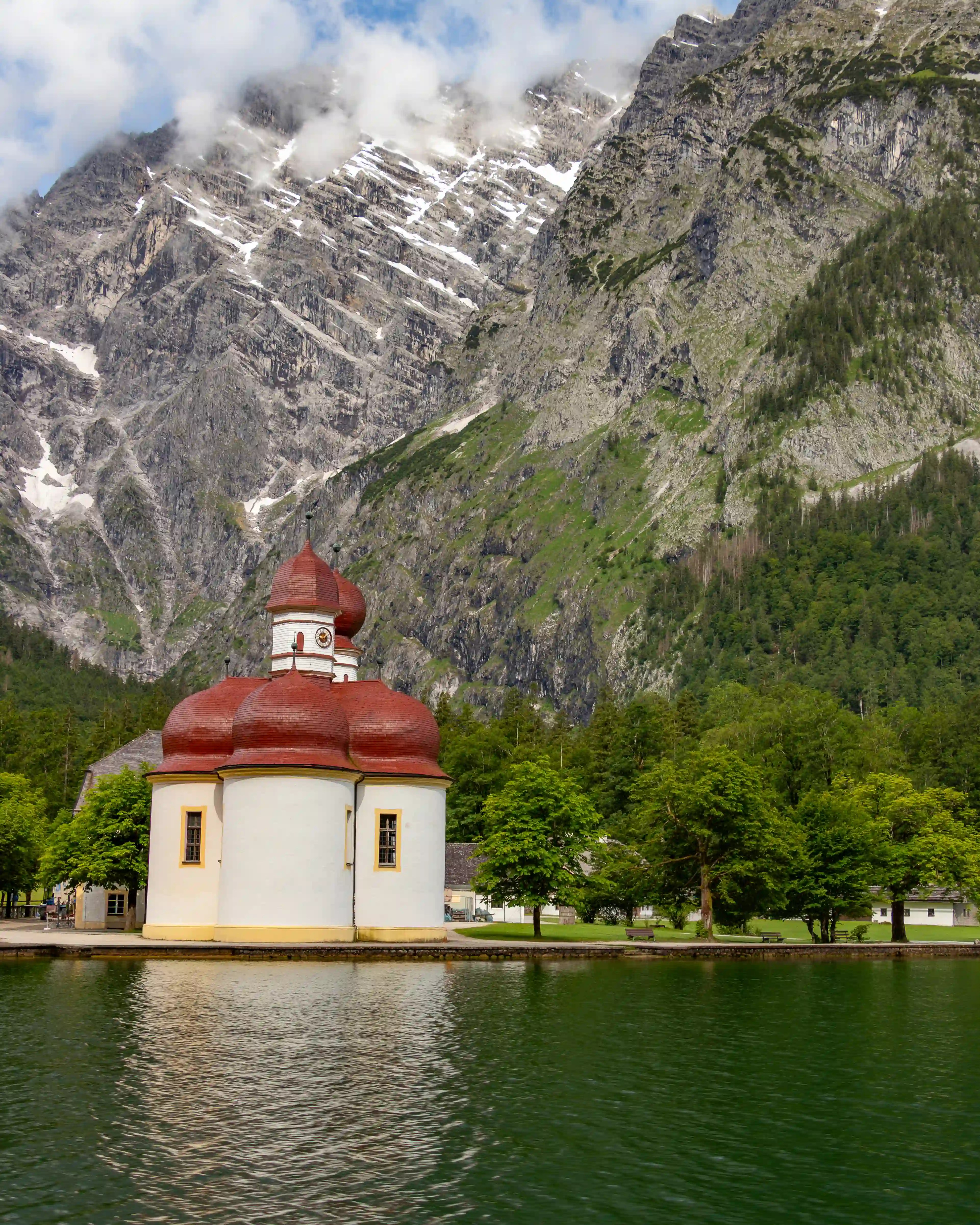 The onion-domed Church of St. Bartholomä sits on the edge of Königssee with steep rocky mountains rising behind it.
