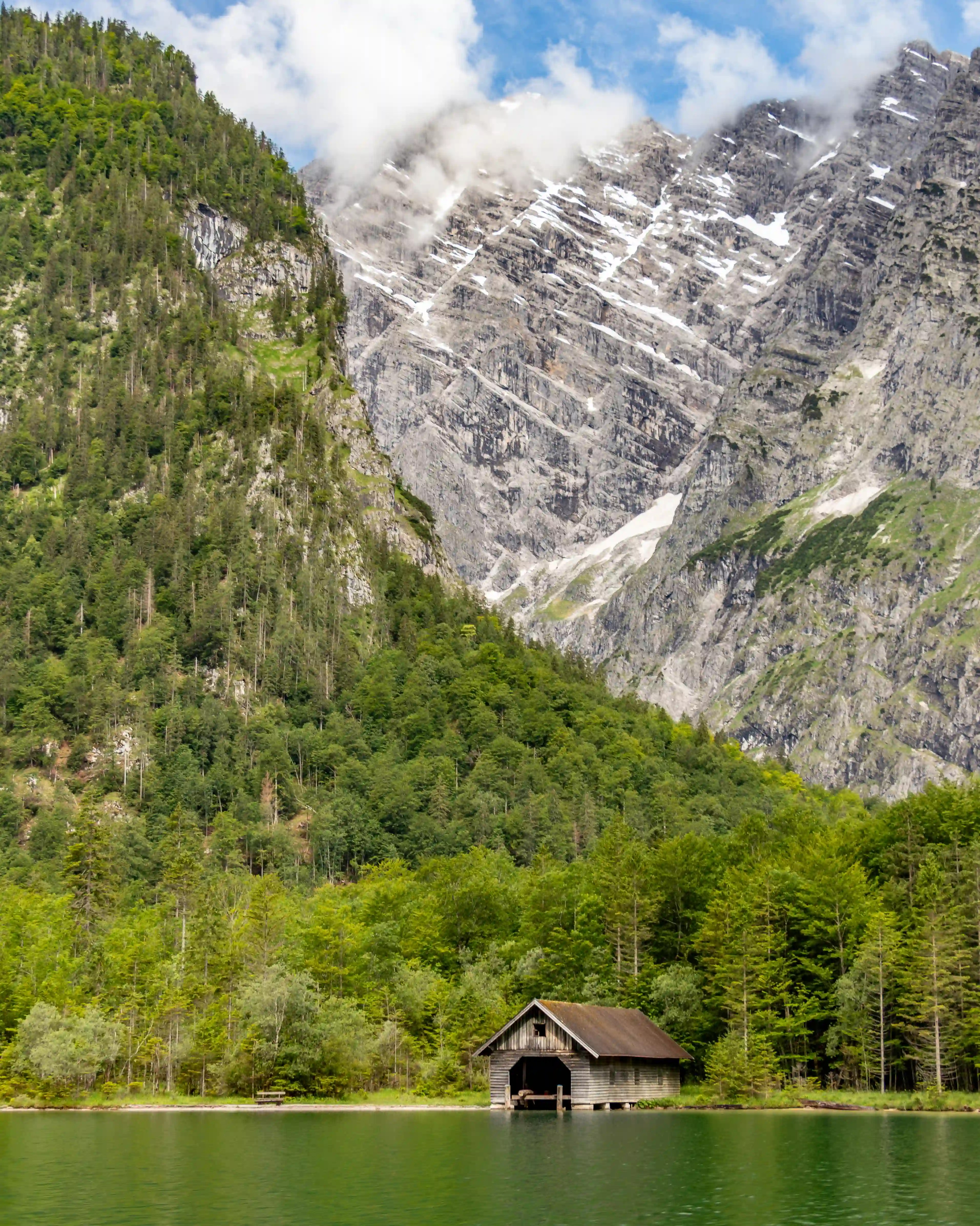 A small wooden boathouse sits at the water’s edge beneath towering forested mountains near the Salet landing on Königssee.