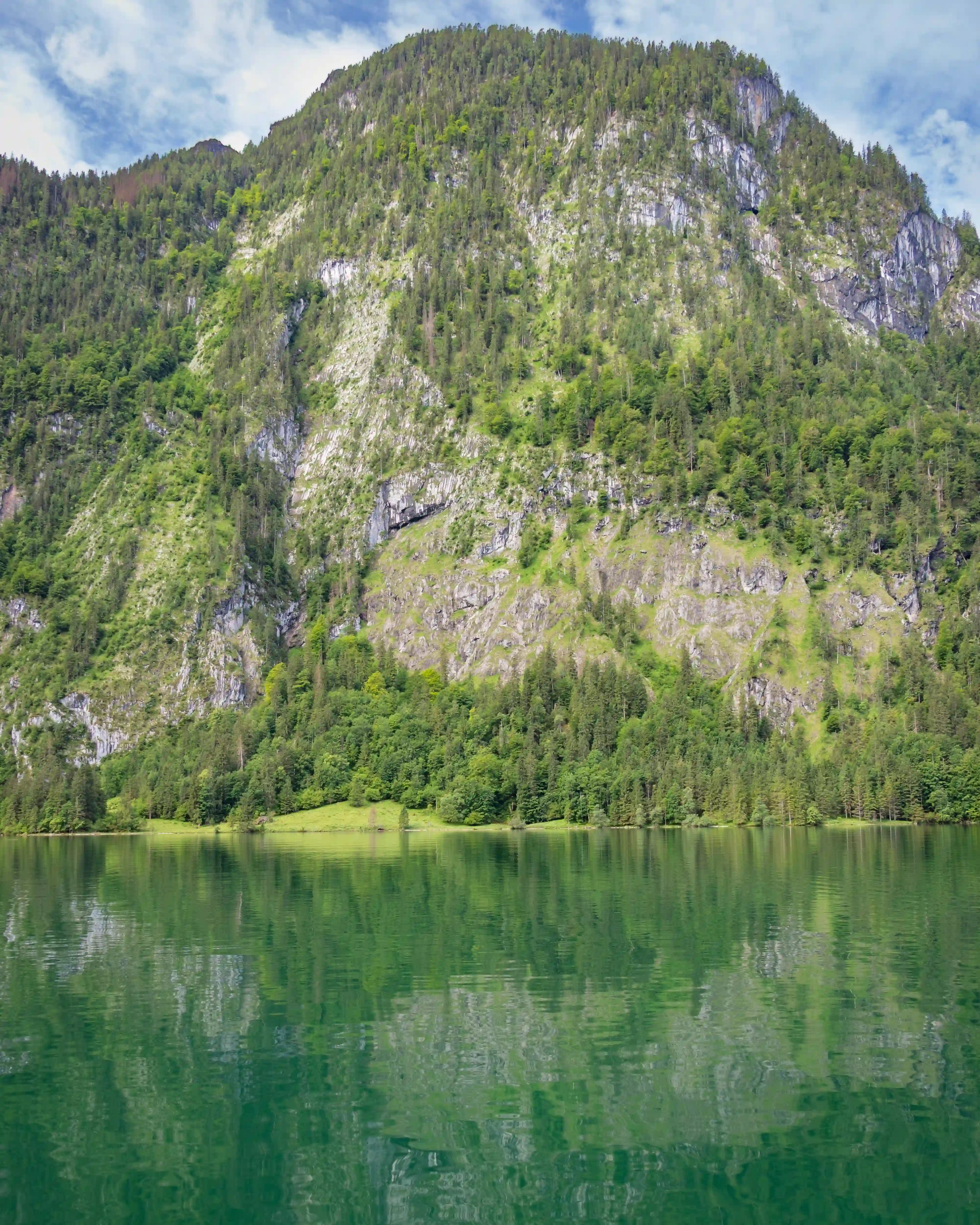 A massive rocky mountainside covered in trees rises steeply from the green waters of Königssee.