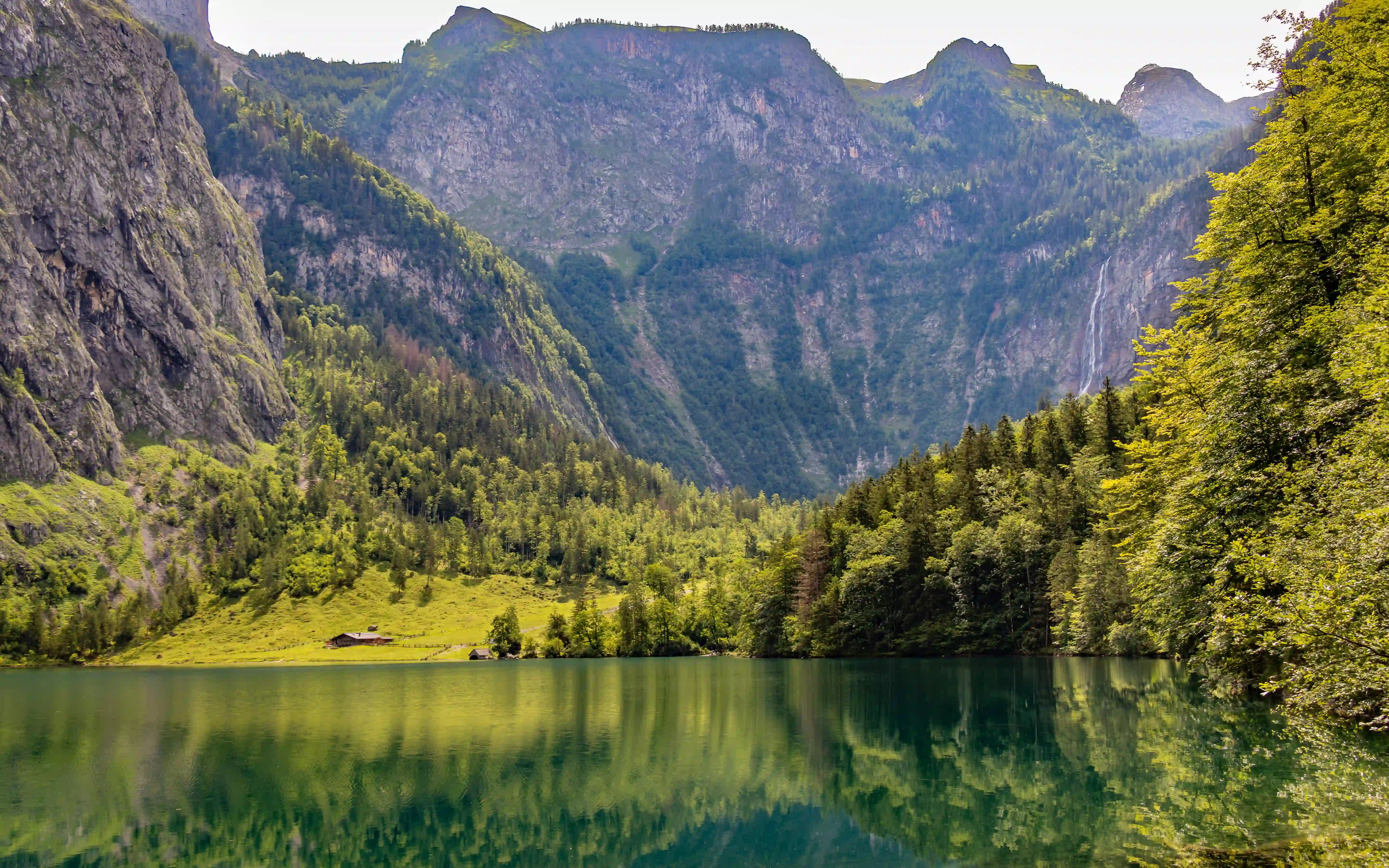 A wide mountain amphitheater surrounds Obersee, with steep cliffs and a bright green meadow reflected in the lake.