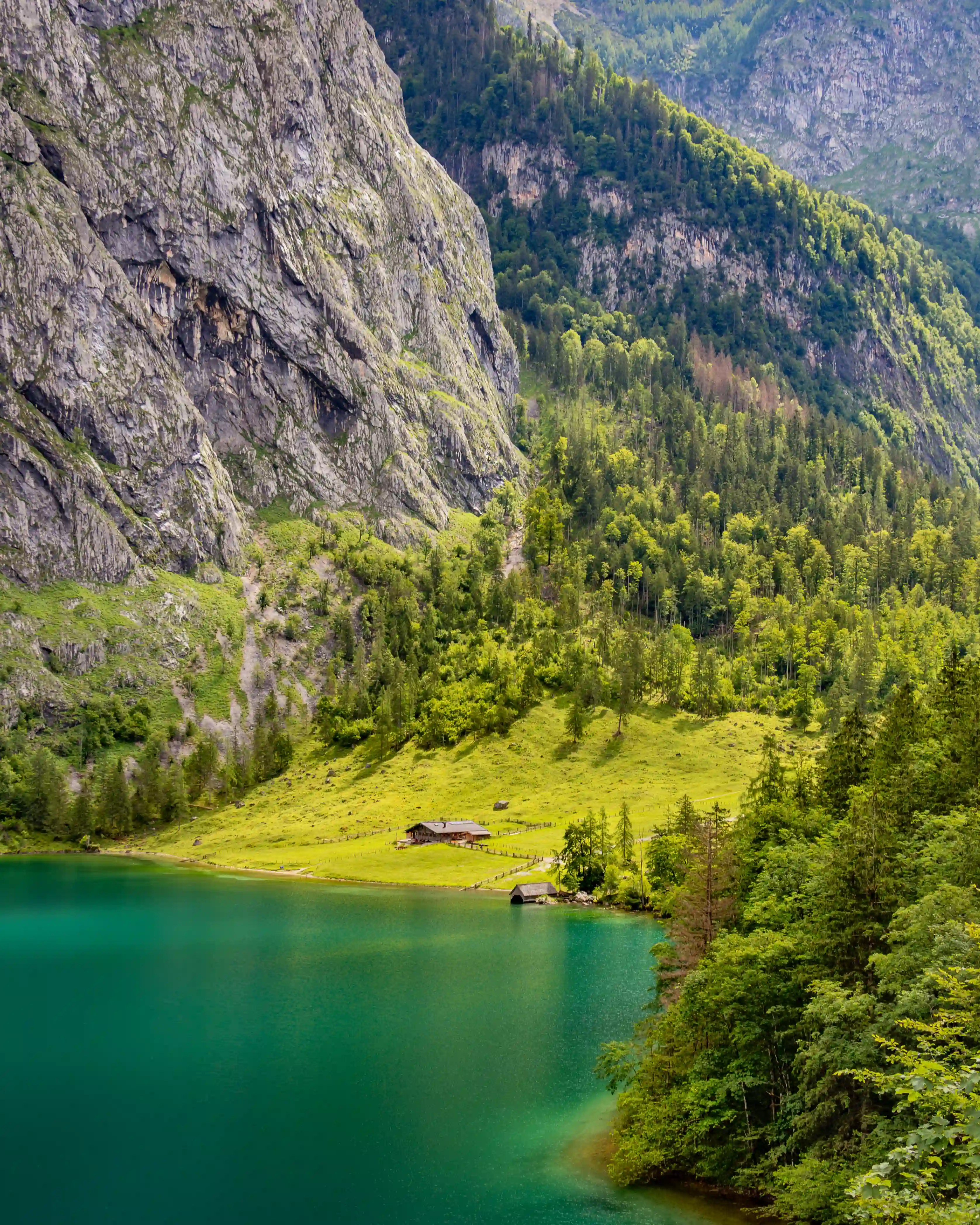 A steep alpine cliff rises above the turquoise waters of Obersee, with a small meadow and wooden hut visible along the shoreline.