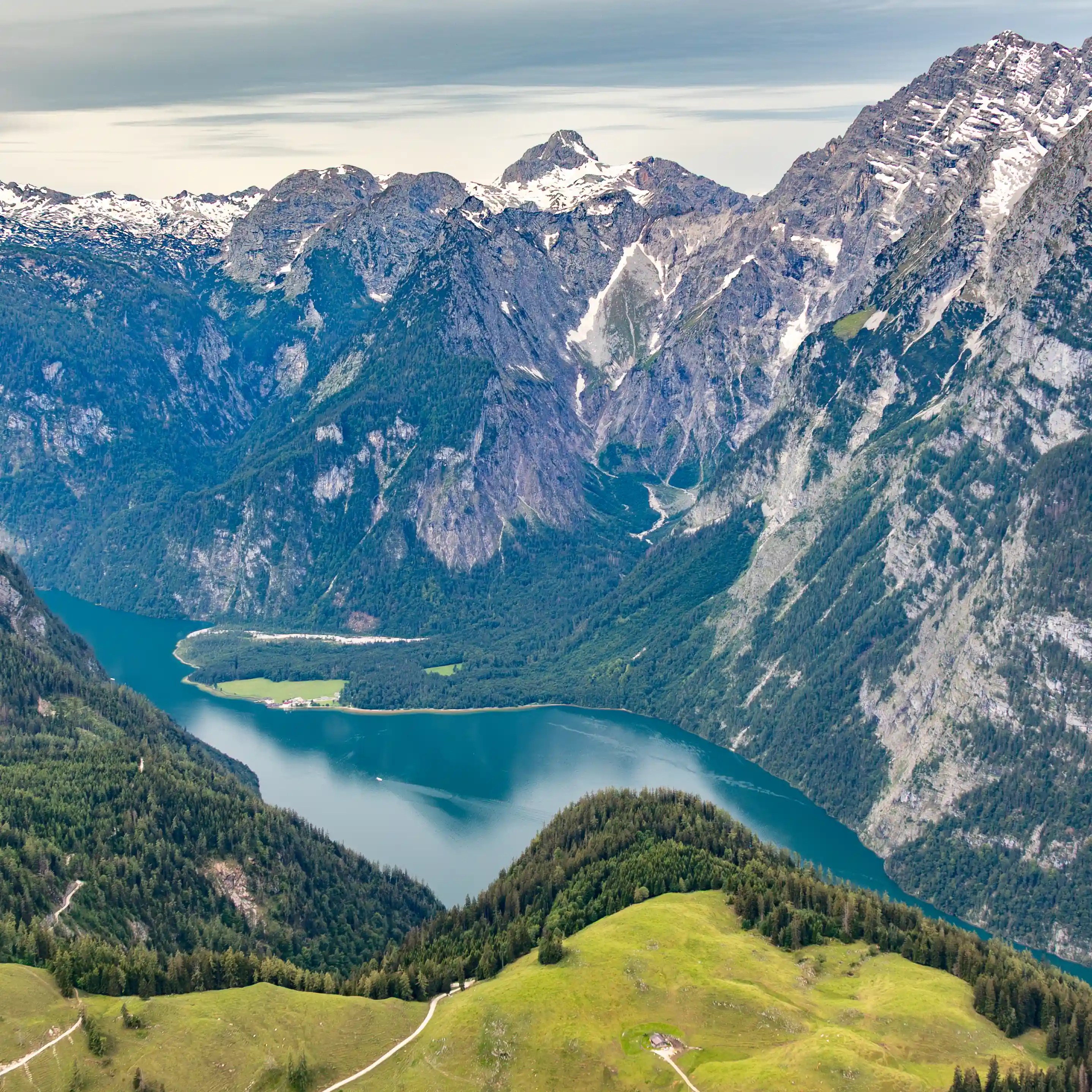 Königssee appears far below as a deep blue lake nestled between steep forested mountains and rocky cliffs.