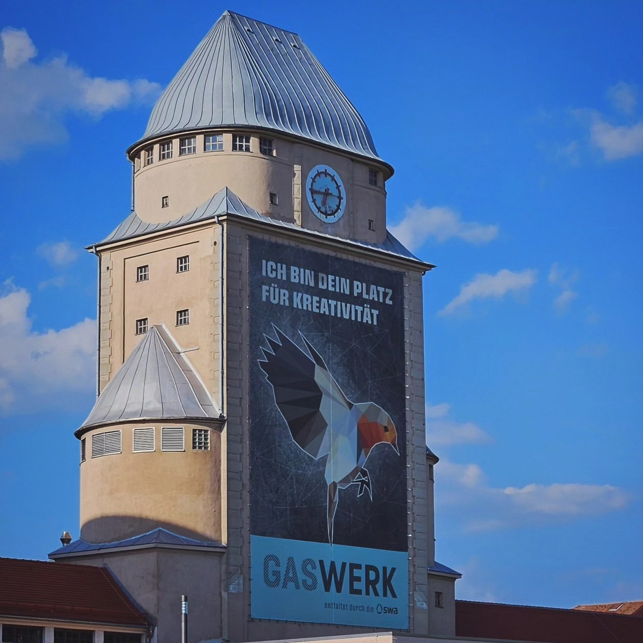 A tall tower at Gaswerk Augsburg with a large mural reading “Ich bin dein Platz für Kreativität” and an illustrated bird.