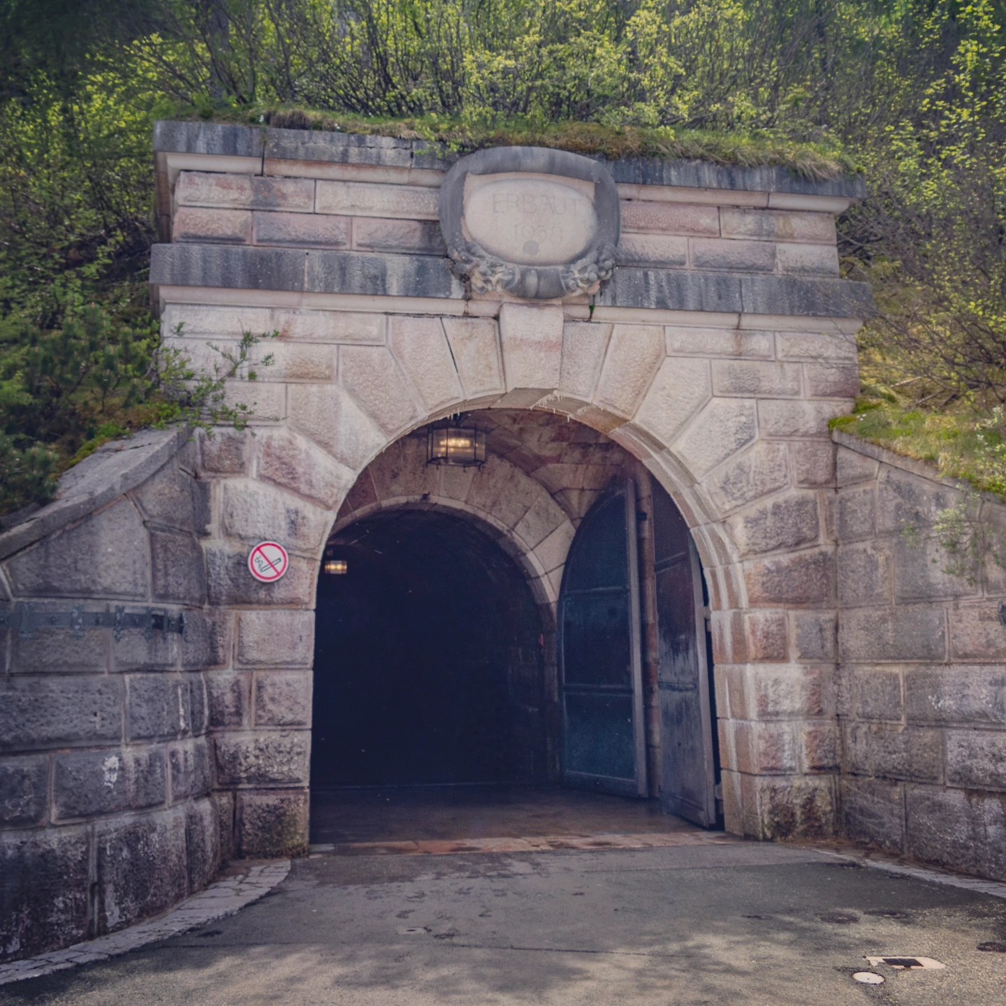 A stone tunnel entrance set into the mountainside with heavy doors and greenery above.
