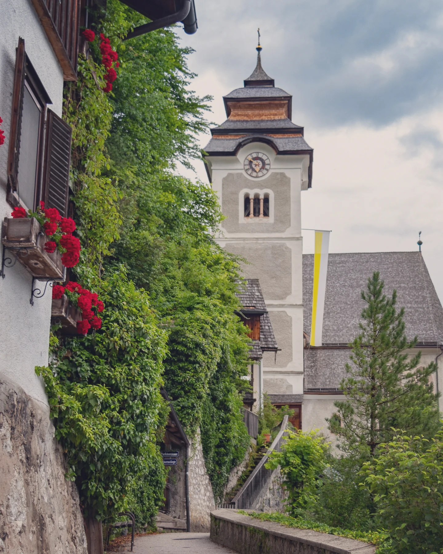 A narrow stone walkway in Hallstatt leading uphill toward a church tower framed by greenery and old buildings.