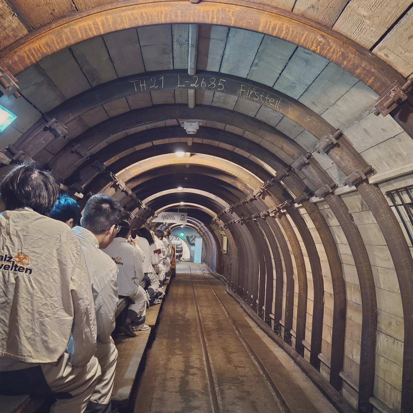 Visitors wearing white protective suits riding a narrow miners’ train through the Hallstatt Salt Mine tunnel.