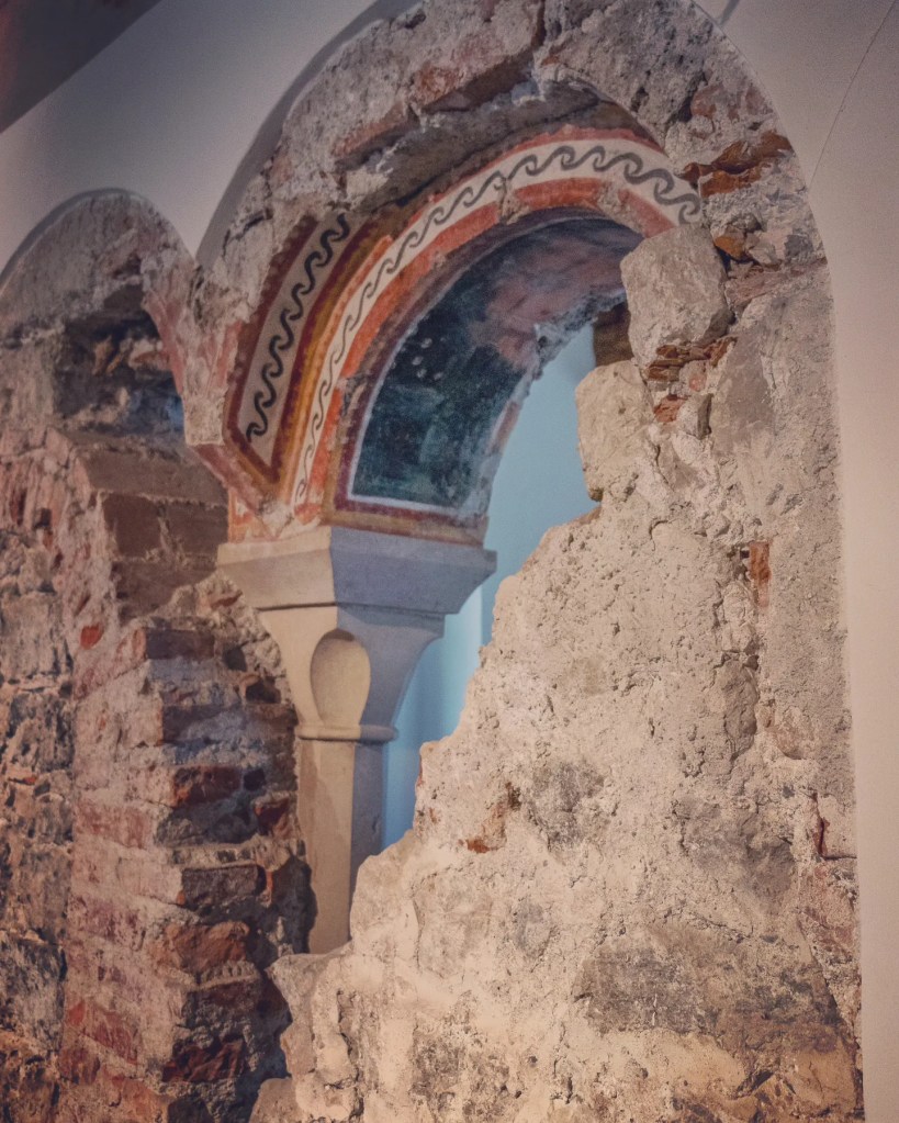 A partially preserved round stone arch with painted decorative patterns set into a thick medieval wall inside Hohensalzburg Fortress.