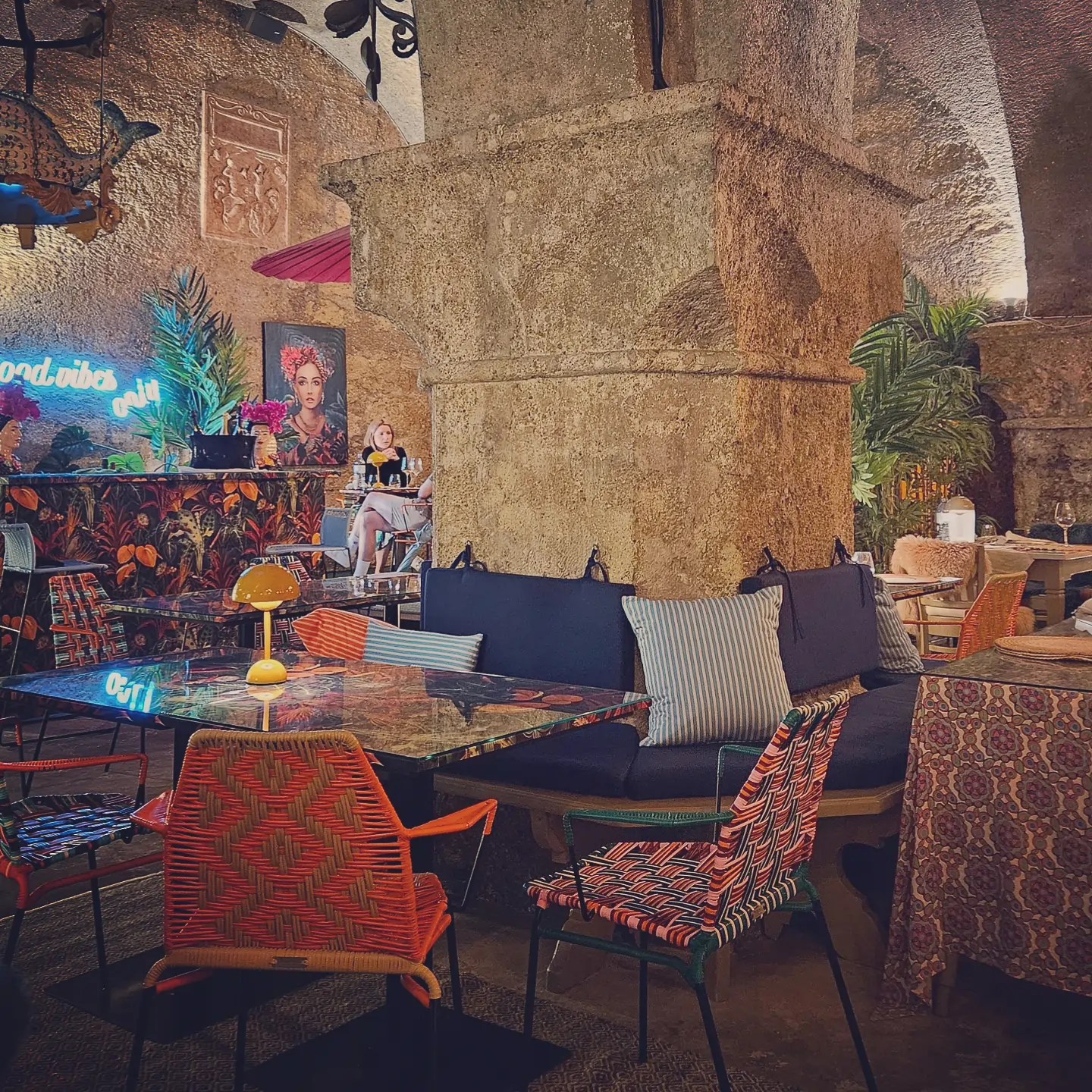 Dining tables and colorful woven chairs arranged around a thick stone pillar inside an arched interior space at St. Peter’s Stiftskulinarium.
