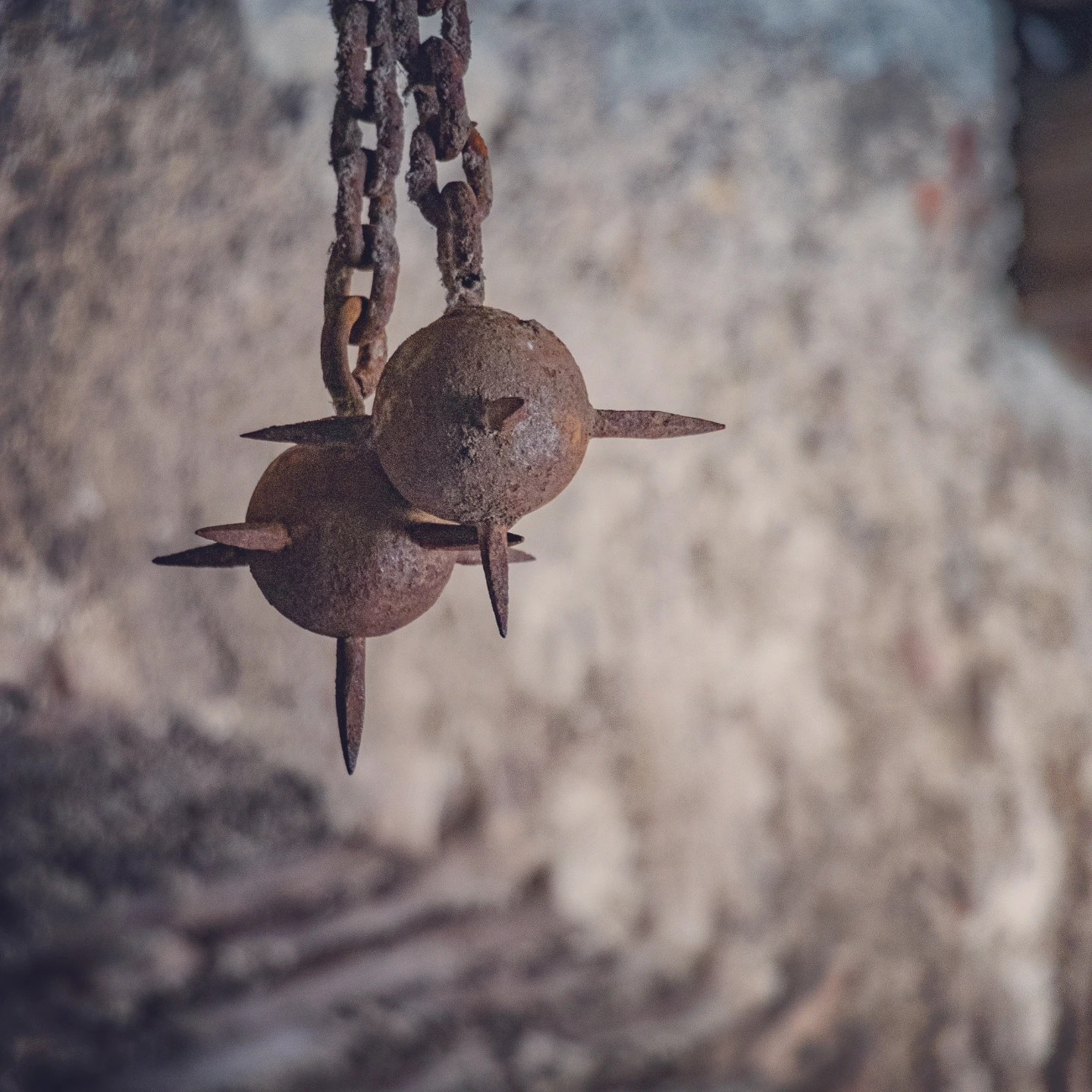 Rusted iron spiked weights hang from chains inside a stone room at Burg Hohenwerfen.
