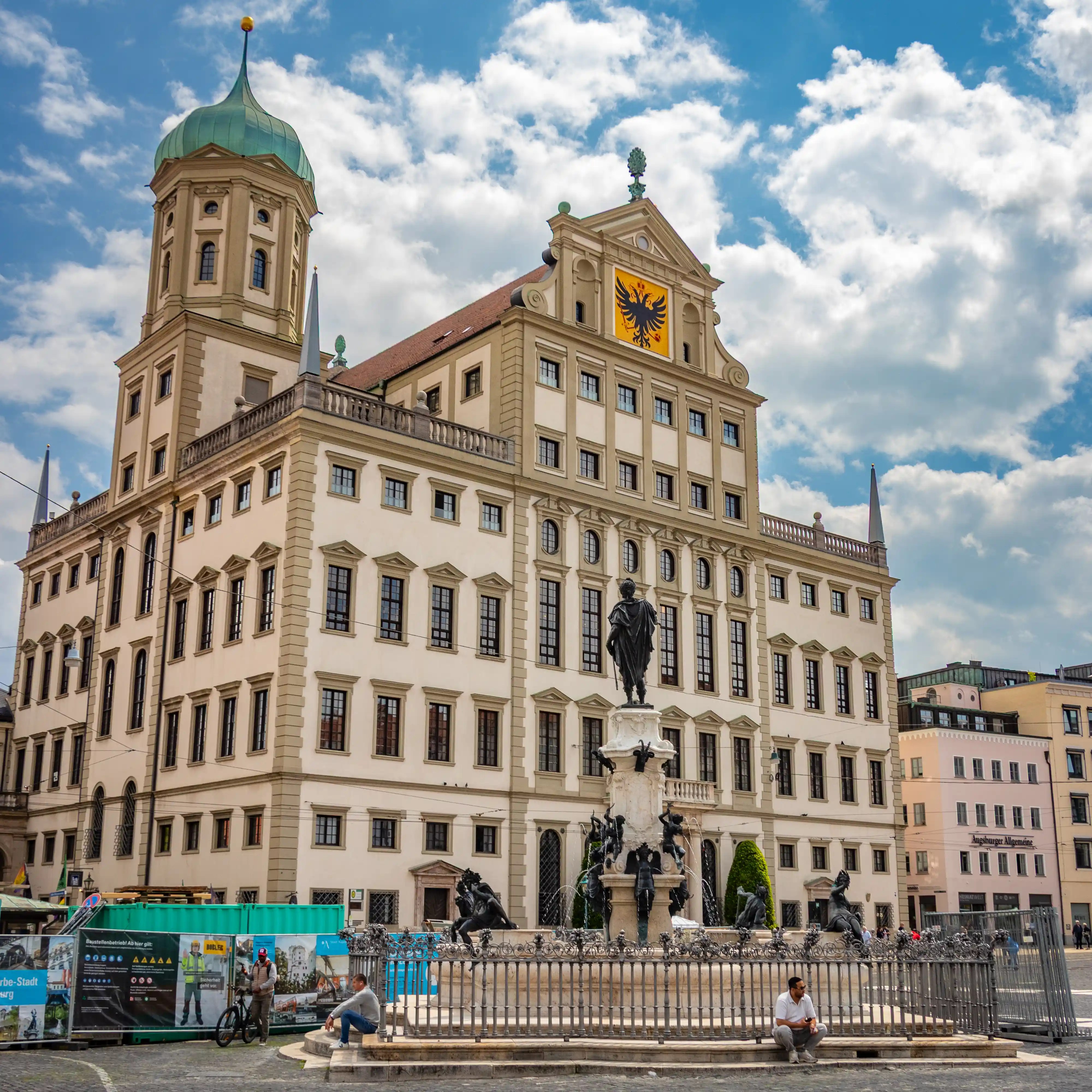 Augsburg Town Hall with the Augustus Fountain in the foreground under a partly cloudy sky.