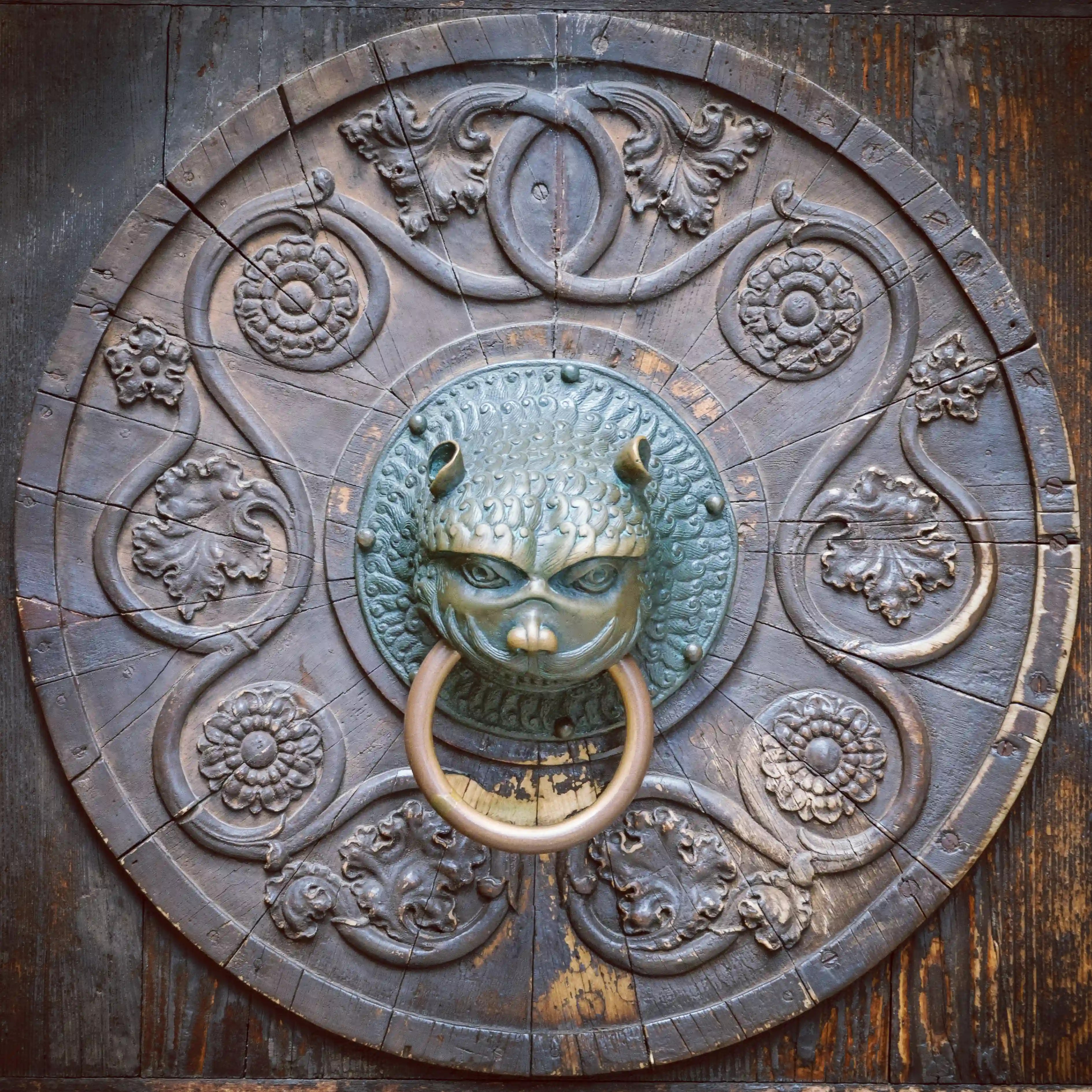 Close-up of an ornate bronze lion-head door knocker set into a carved wooden door in Augsburg.