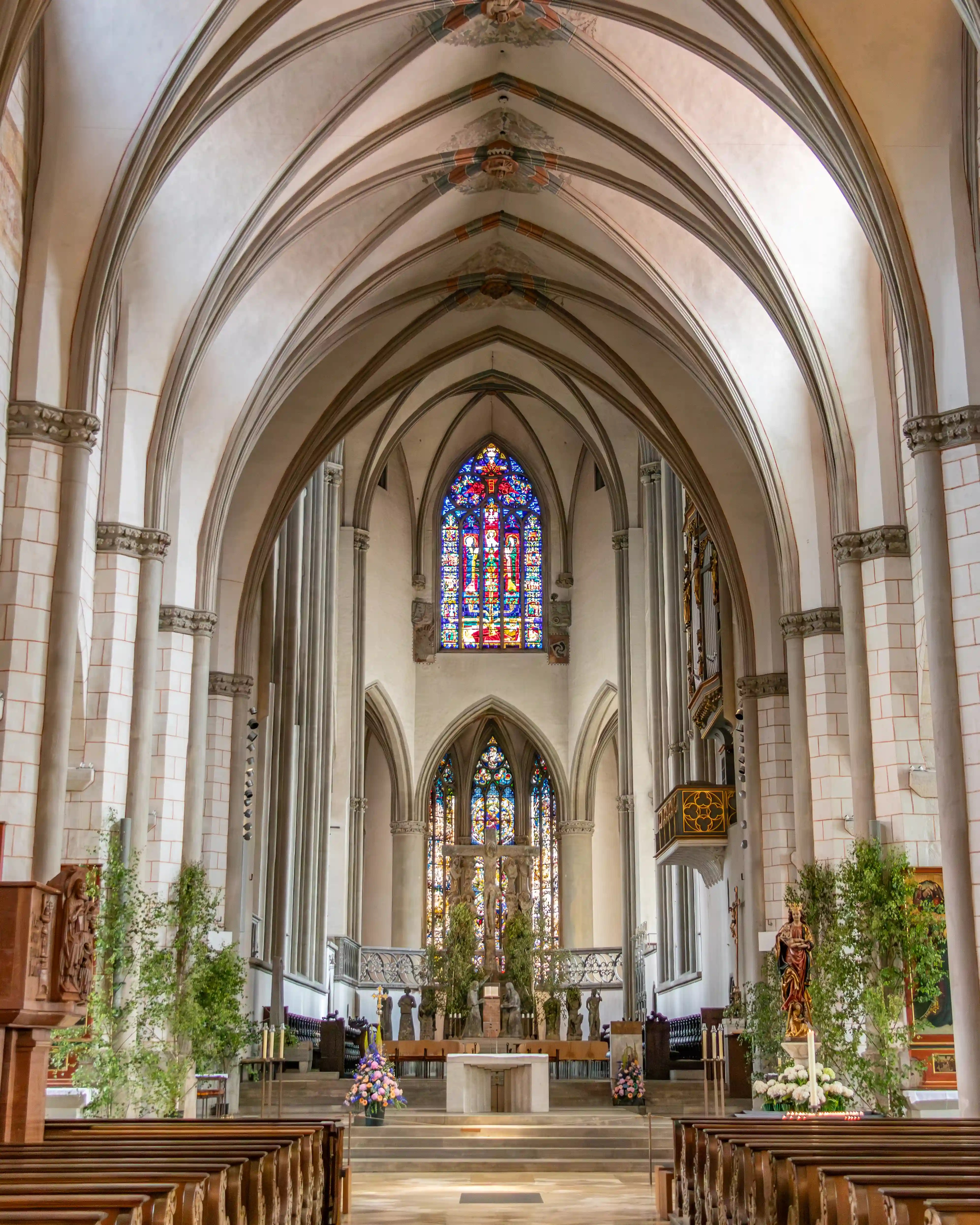 The interior of Augsburg Cathedral showing tall Gothic arches, rows of pews, and stained glass windows behind the altar.