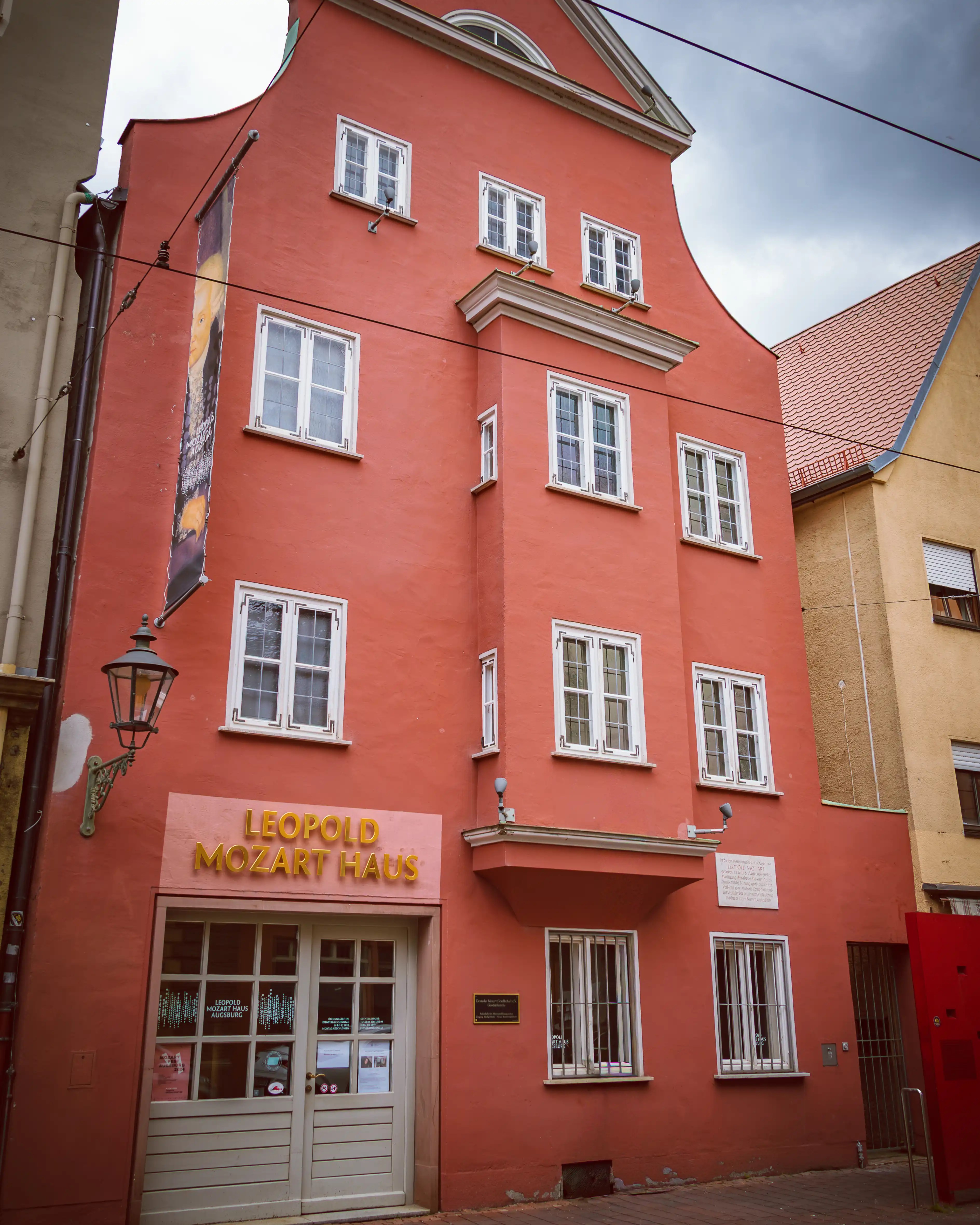A tall red historic building in Augsburg with white-trimmed windows and a sign reading “Leopold Mozart Haus” above the entrance.
