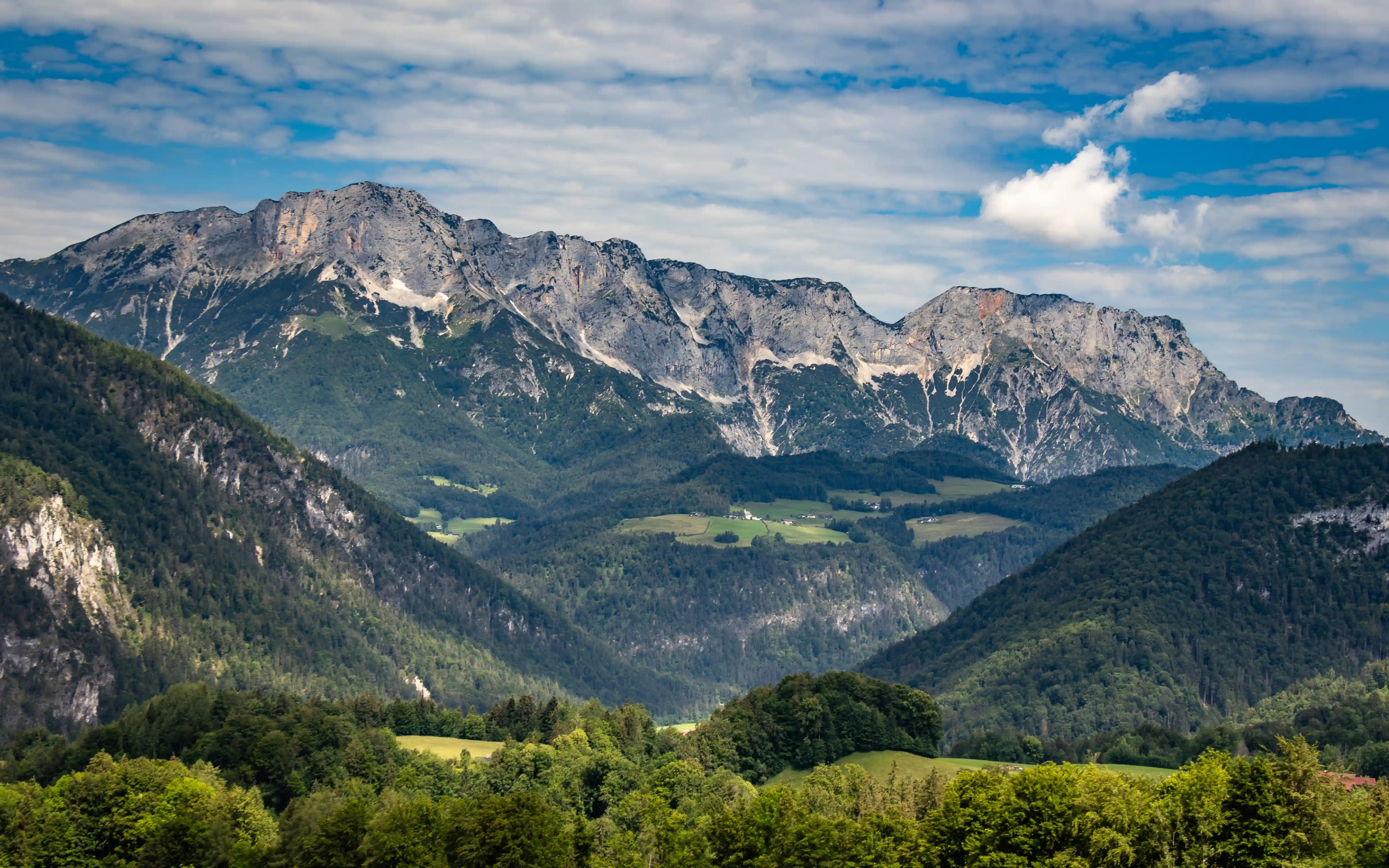 A wide view of rugged alpine mountains rising above green valleys under a partly cloudy sky near the Eagle’s Nest.