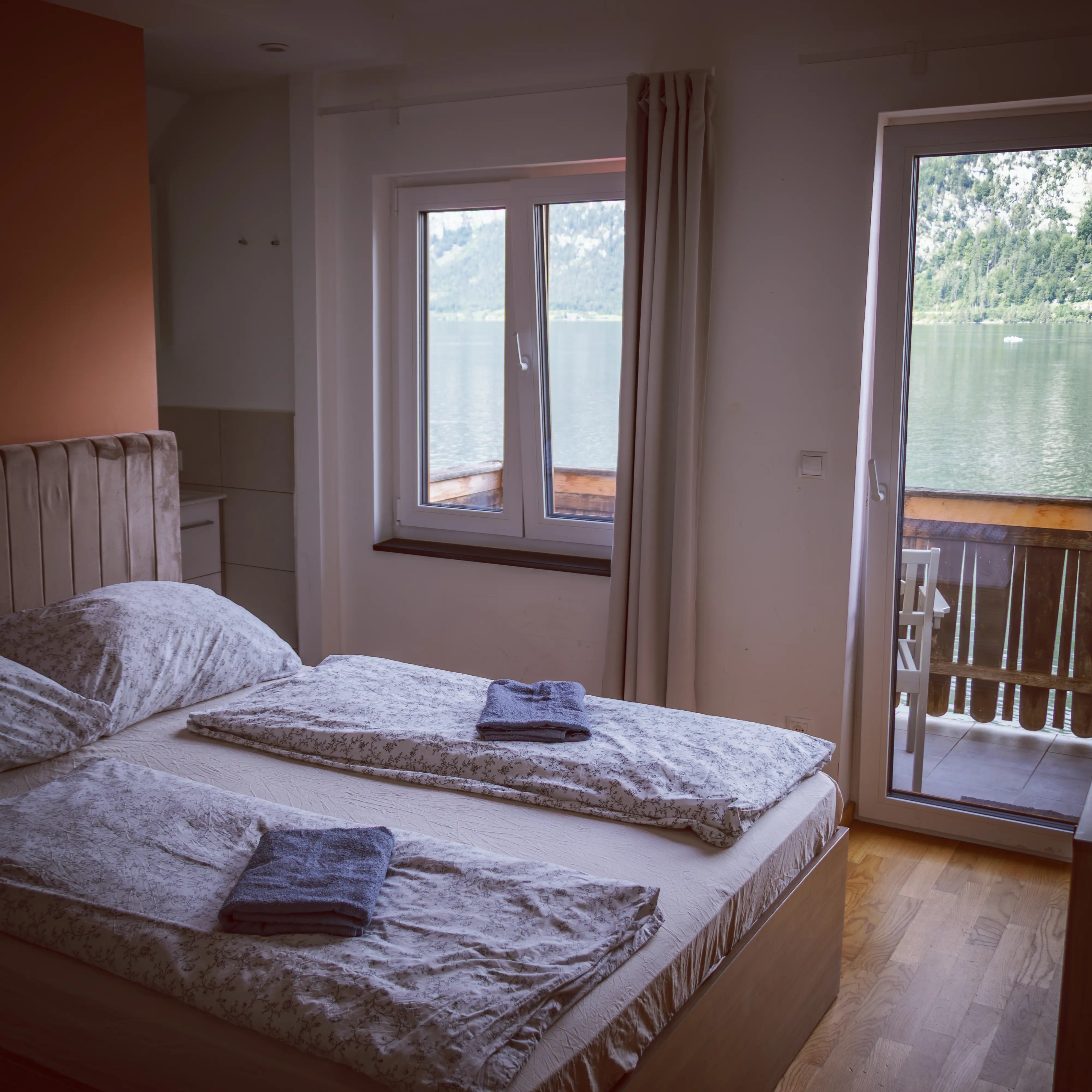 A bedroom with a full bed looks out through a window toward Hallstatt Lake.