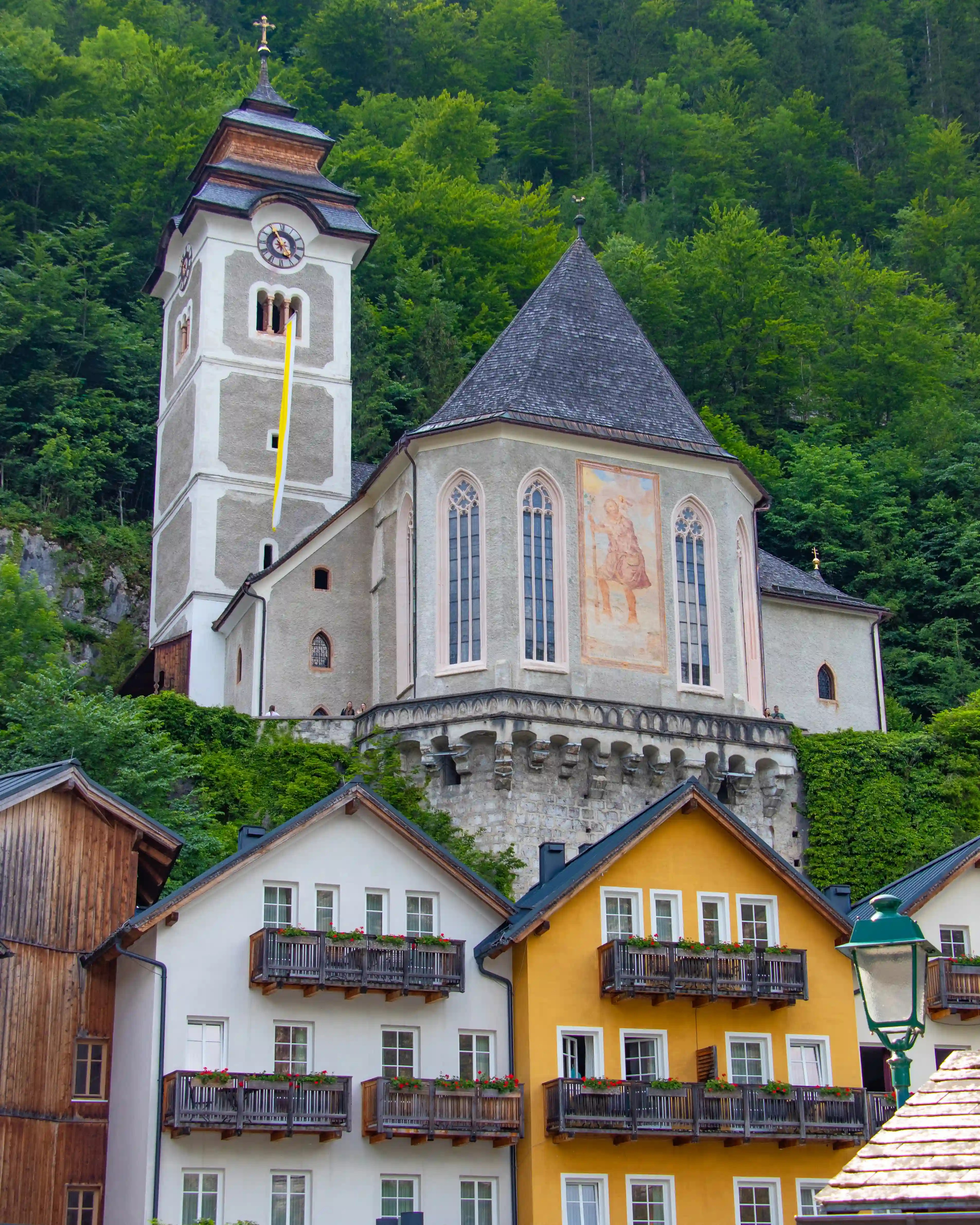 The Hallstatt parish church perched above colorful houses with forested mountains in the background.