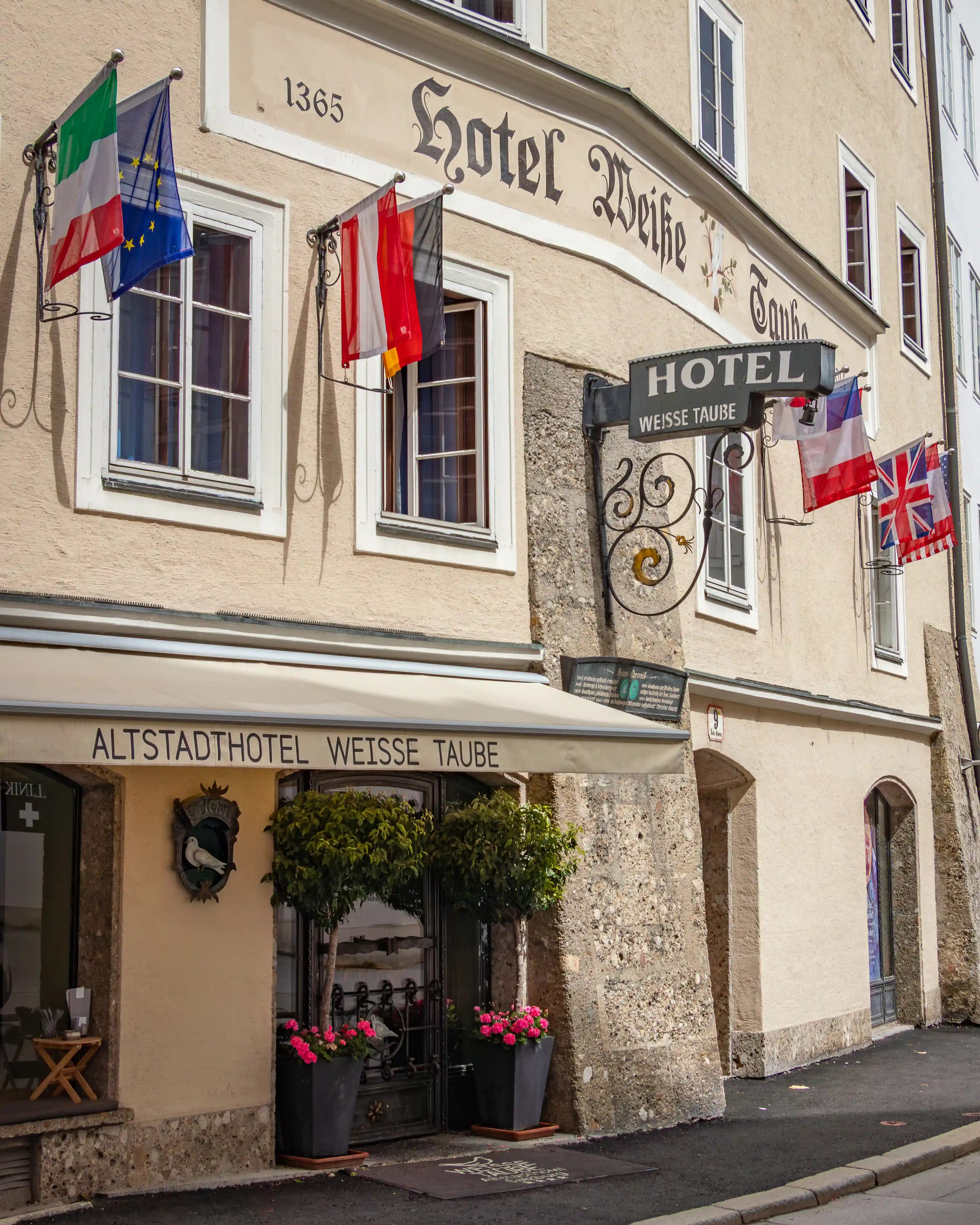 The exterior of Altstadthotel Weisse Taube in Salzburg’s Old Town, with flags hanging above the entrance and historic lettering on the facade.