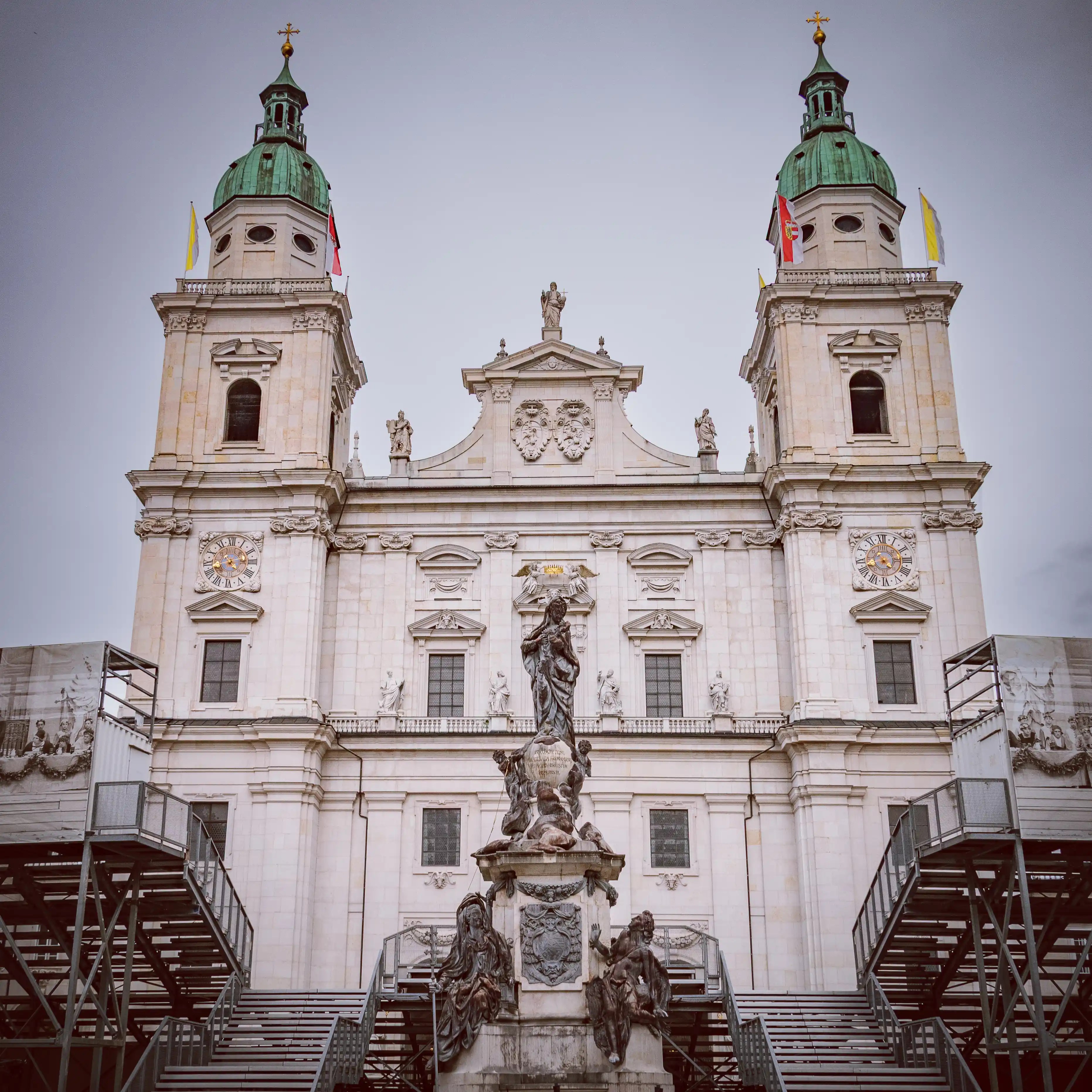 The Baroque façade of Salzburg Cathedral with its twin green domed towers rises behind the Marian Column statue in the cathedral square.