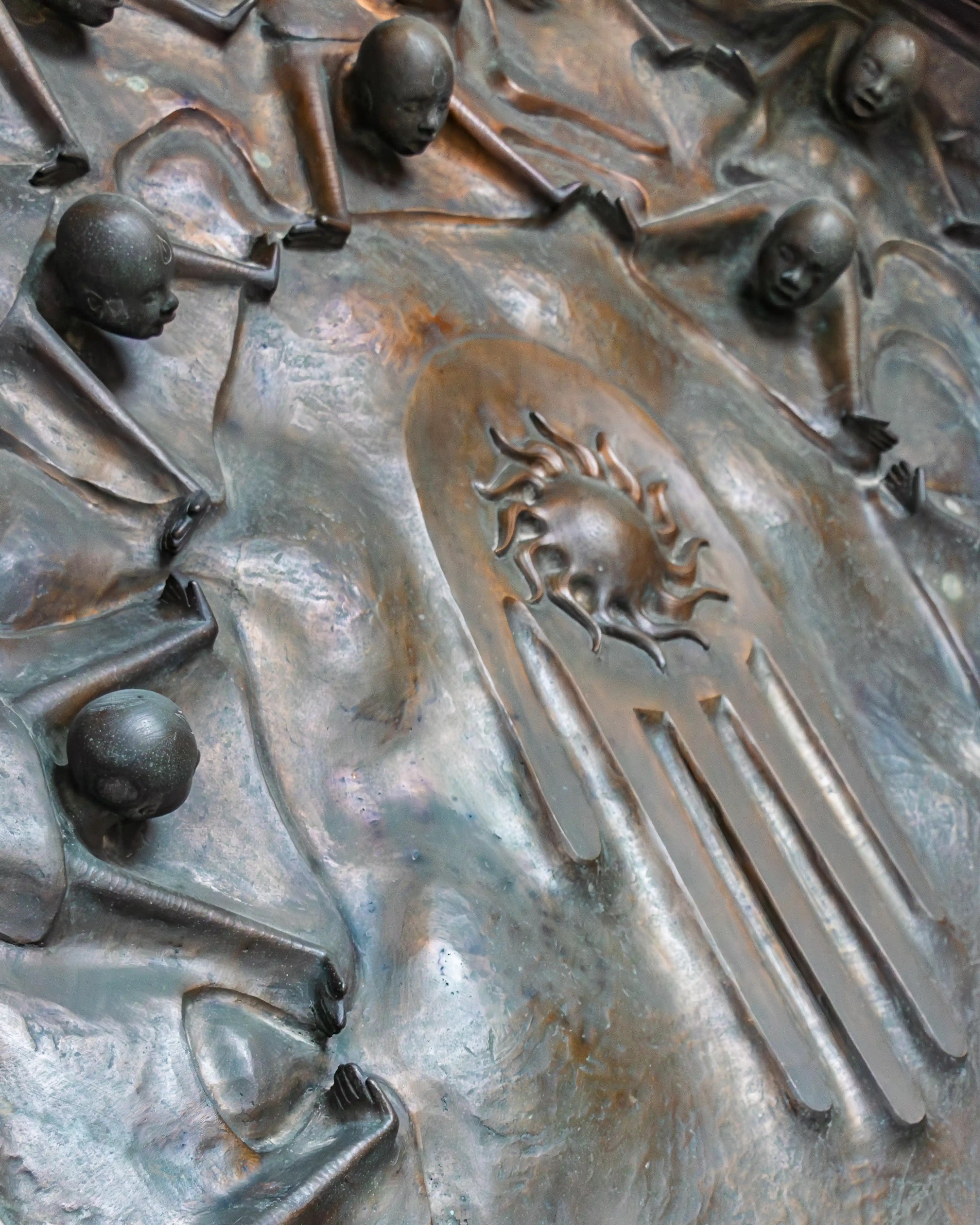 A close-up of the bronze relief on the Door of Hope at Salzburg Cathedral, showing small sculpted human figures emerging from textured metal around symbolic imagery.