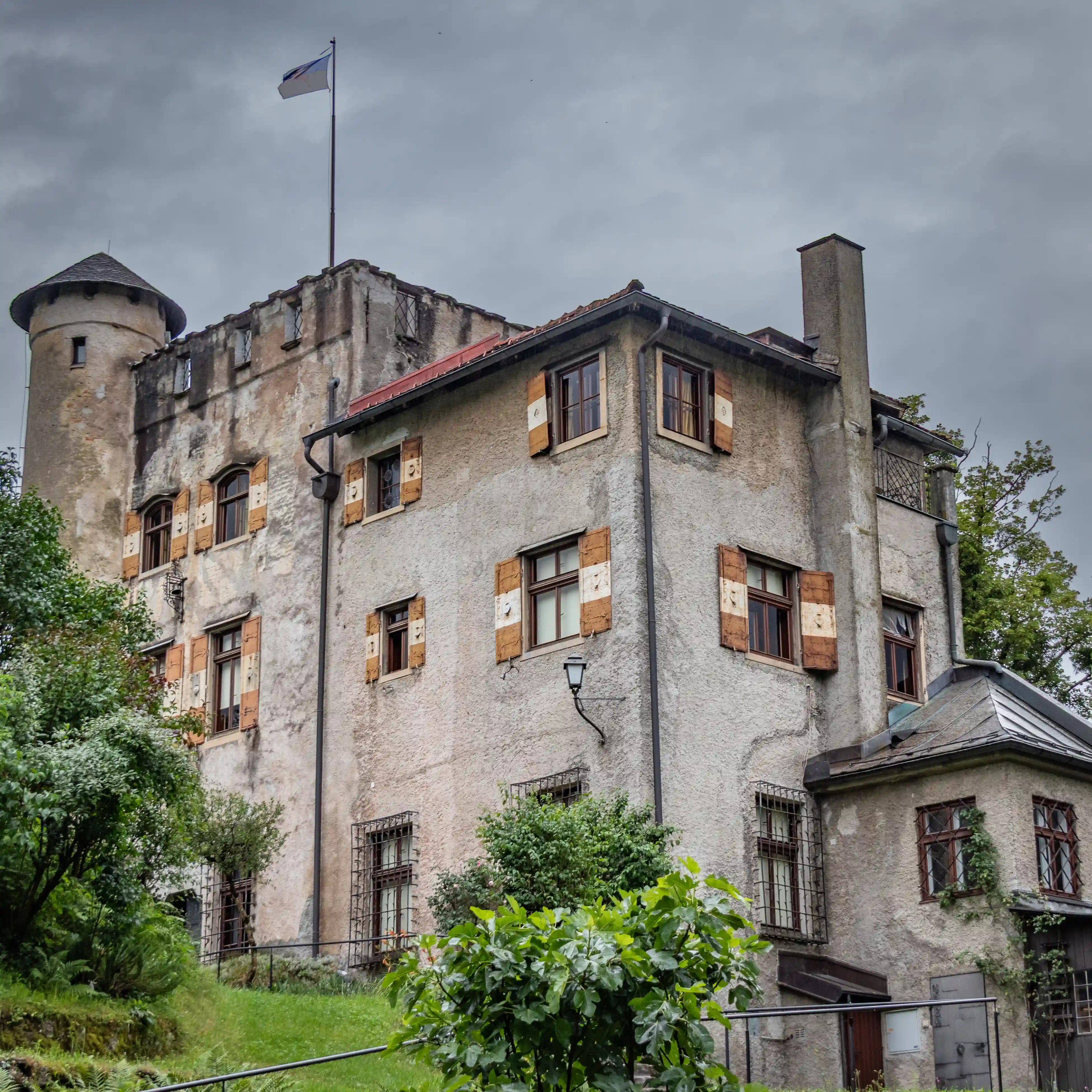 A historic stone building with shuttered windows and a small tower, set into the greenery near the Mönchsberg fortifications.