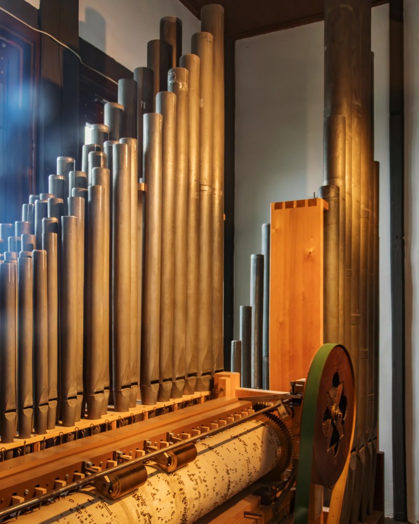 A close-up view of the Salzburg Bull mechanical organ inside Hohensalzburg Fortress, showing tall metal organ pipes and a wooden barrel mechanism used to play music.
