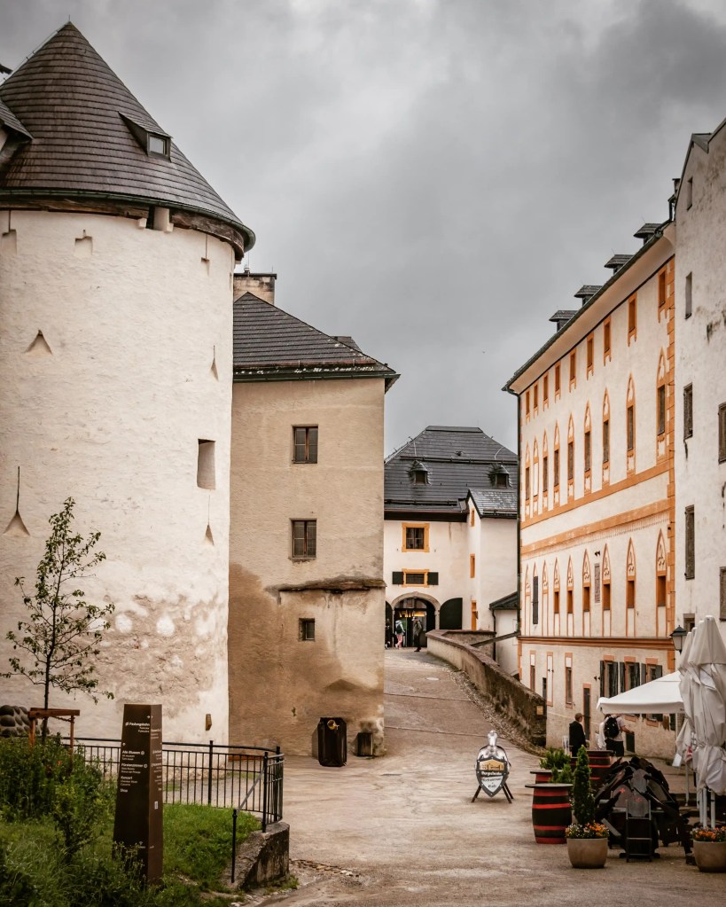 A narrow stone lane runs between tall fortress buildings, with arched doorways and a small sign near the path.