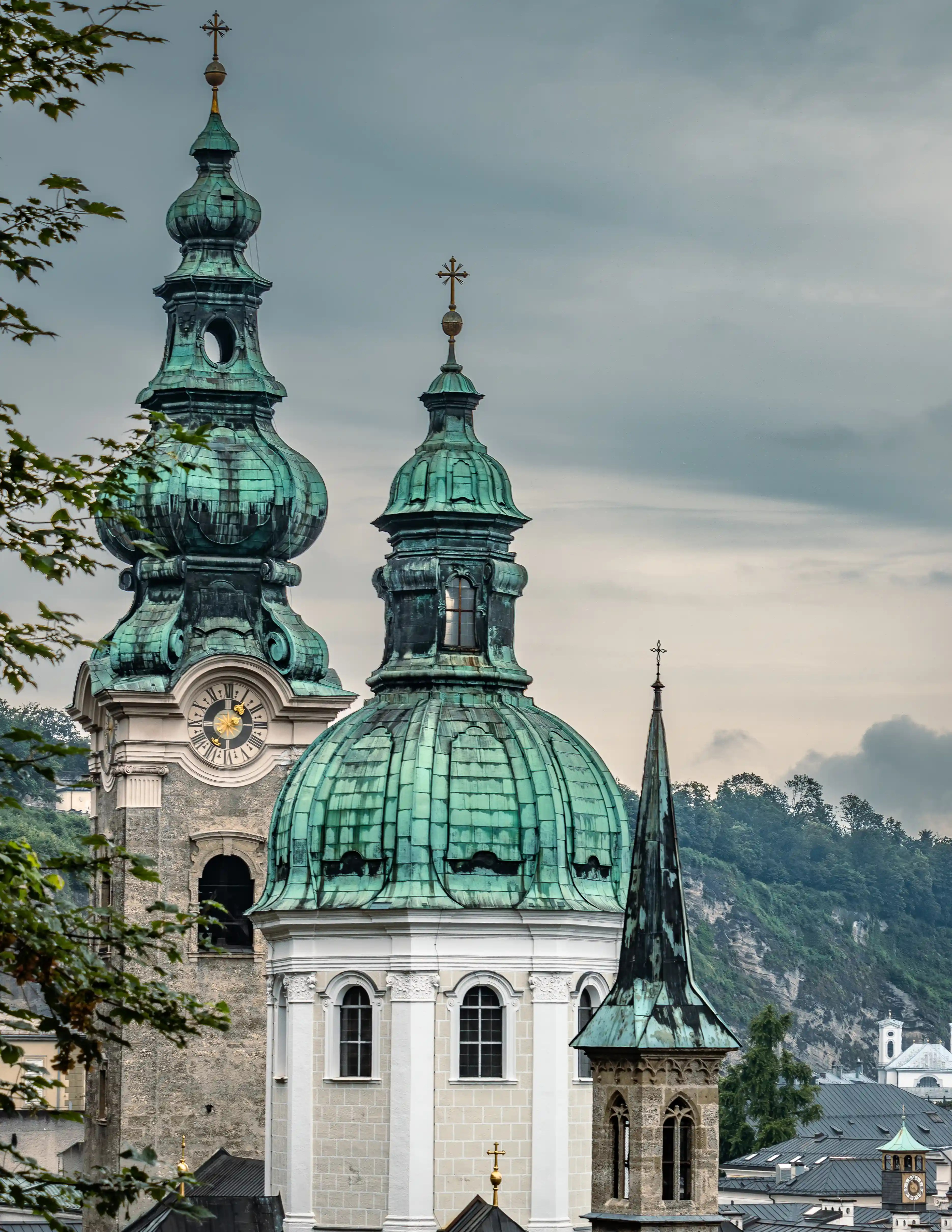 Copper-green church domes and towers rising above Salzburg’s Old Town rooftops with wooded hills in the background.