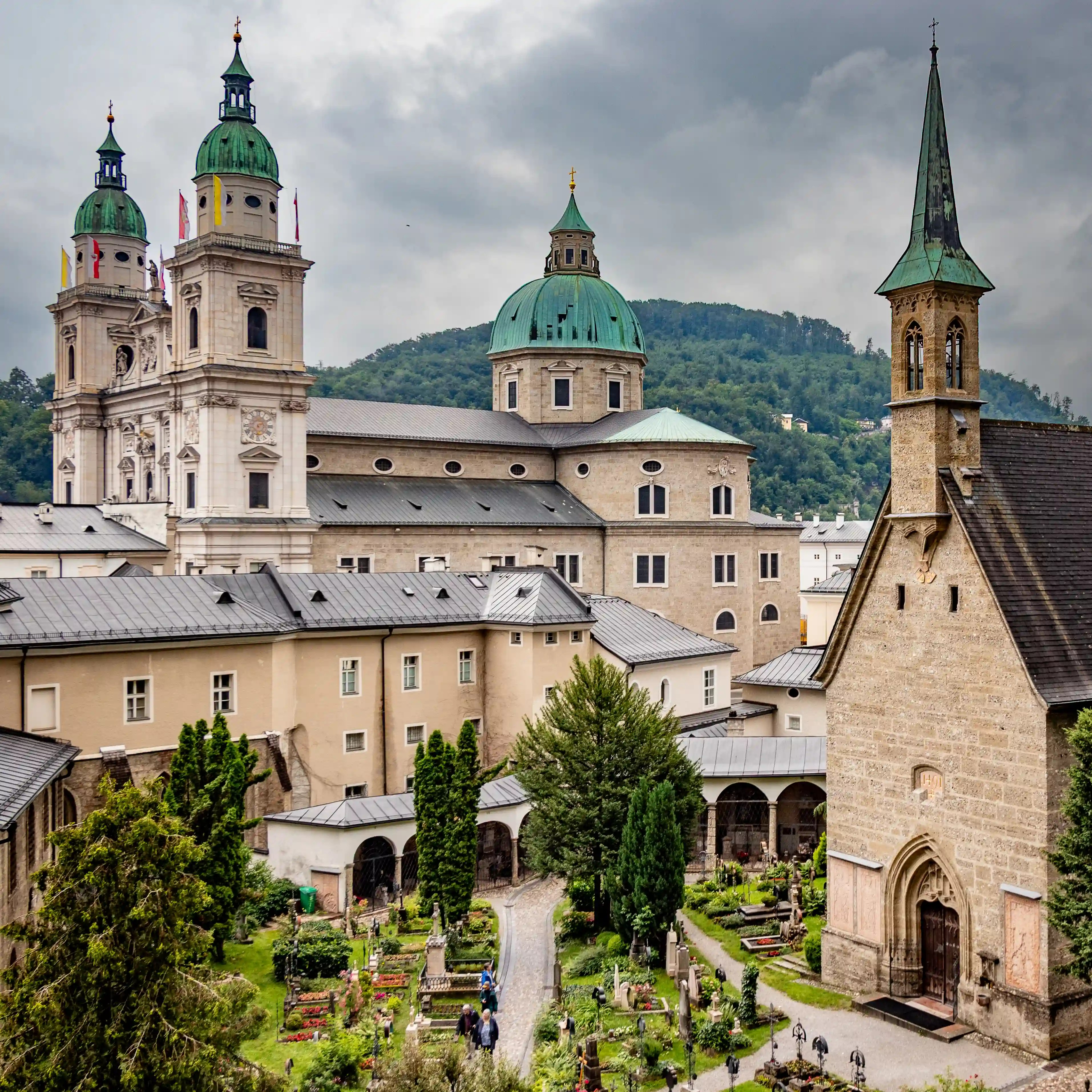 A view over St. Peter’s Cemetery shows St. Margaret's Chapel, gravestones, and Salzburg Cathedral rising behind it.