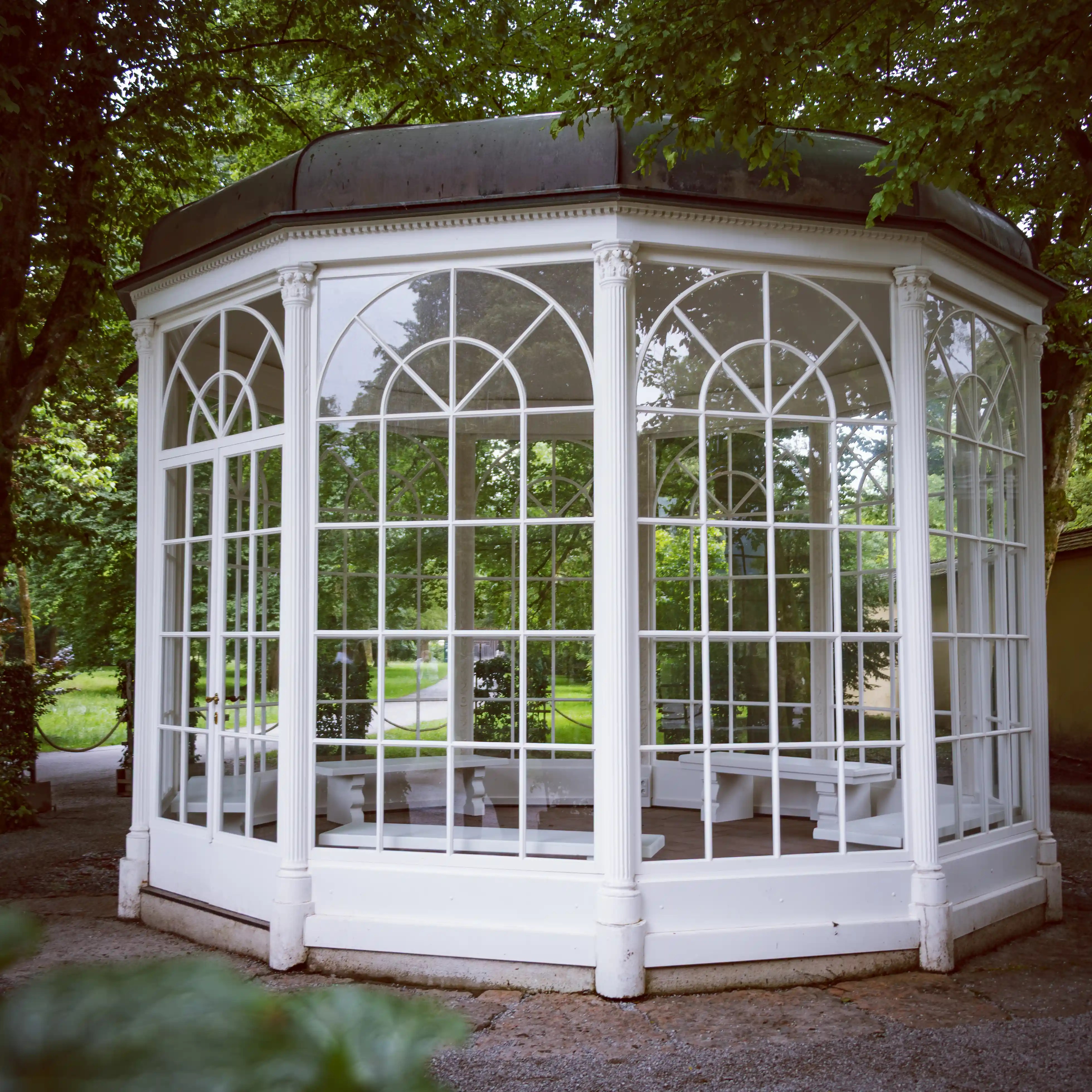 A white octagonal gazebo with arched windows stands among trees in Hellbrunn Palace Park.