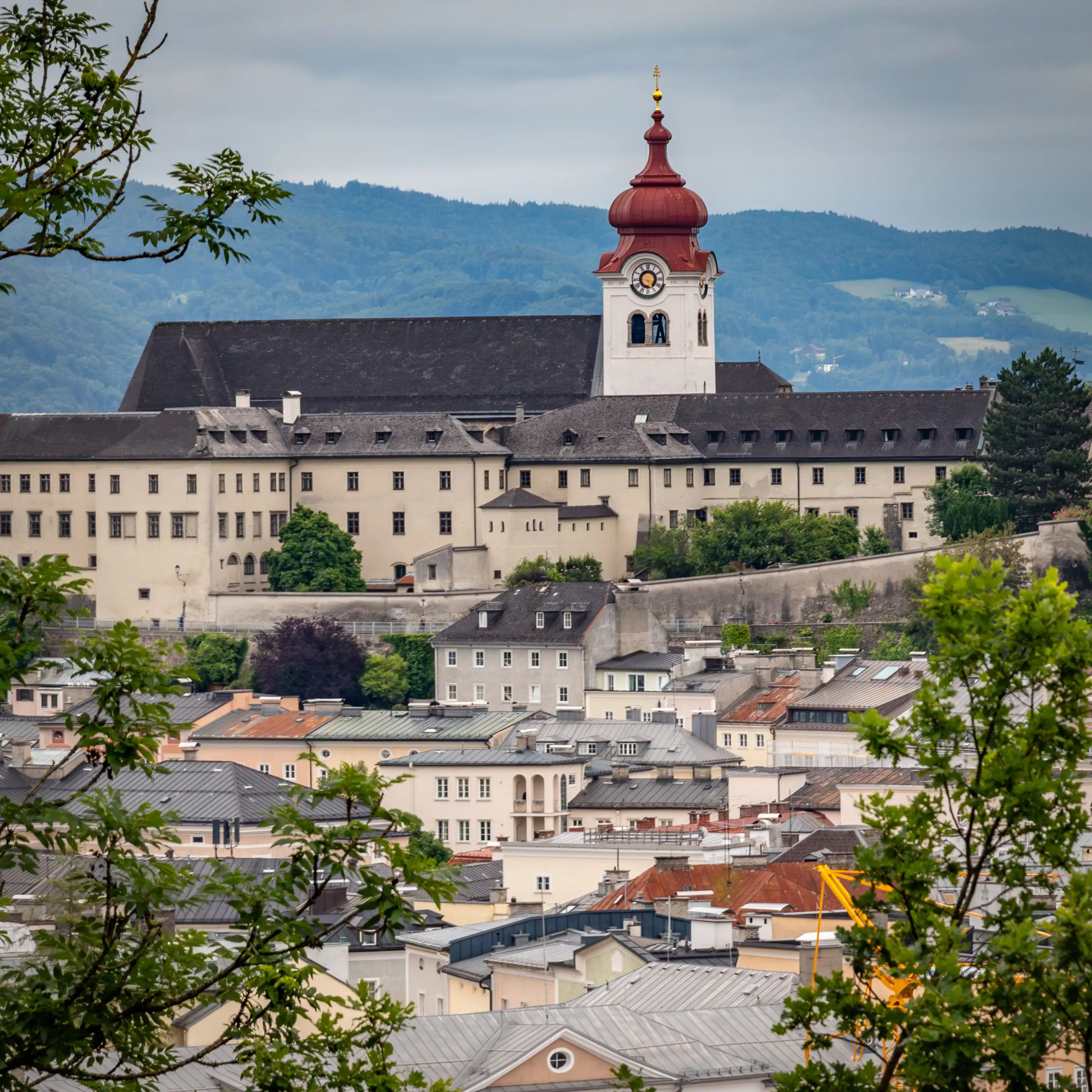 Salzburg Nonnberg Abbey seen from above the Old Town, with its long pale buildings and red-domed clock tower set against forested hills.