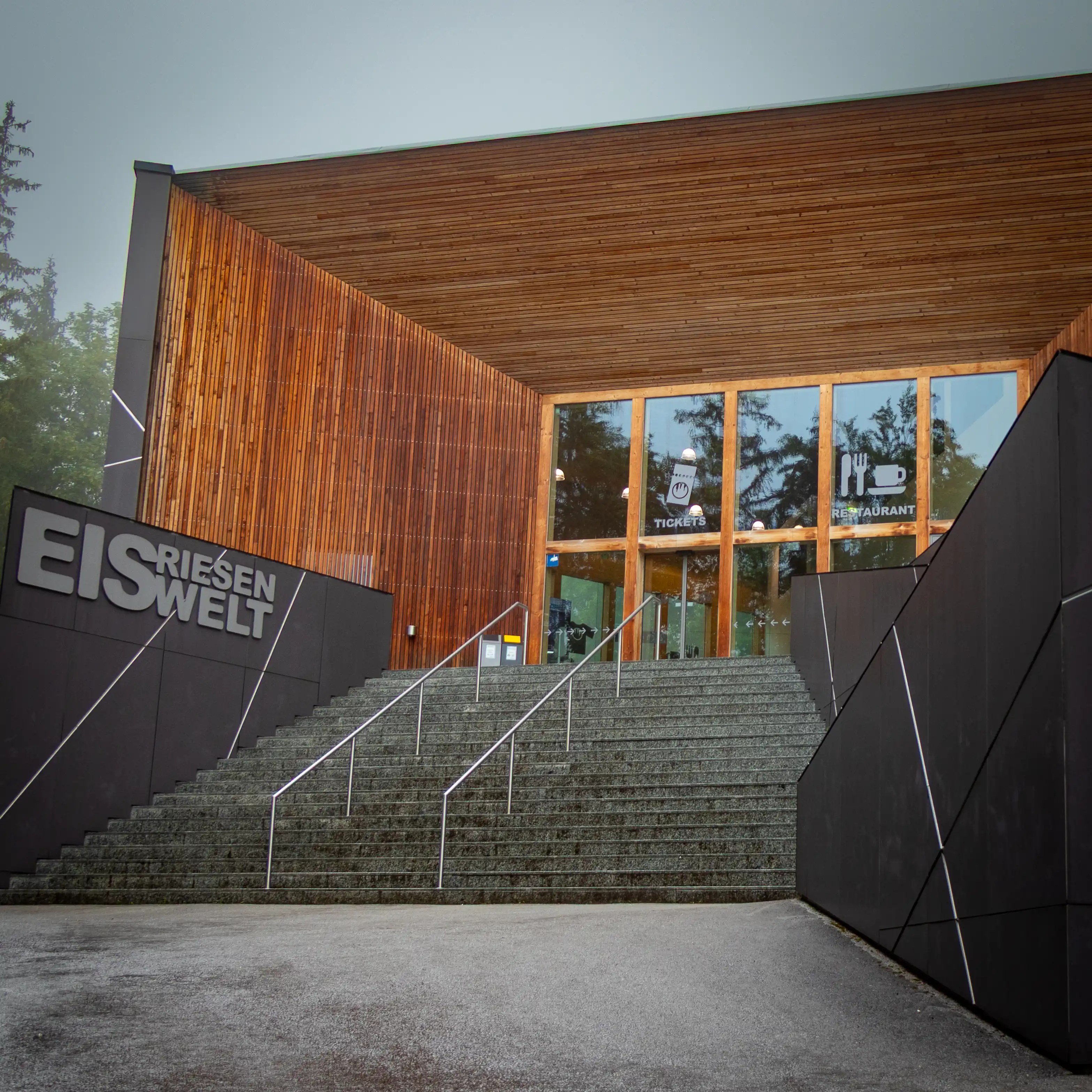 The modern Eisriesenwelt visitor center with wide stone steps leading up to a wooden building on a foggy day.