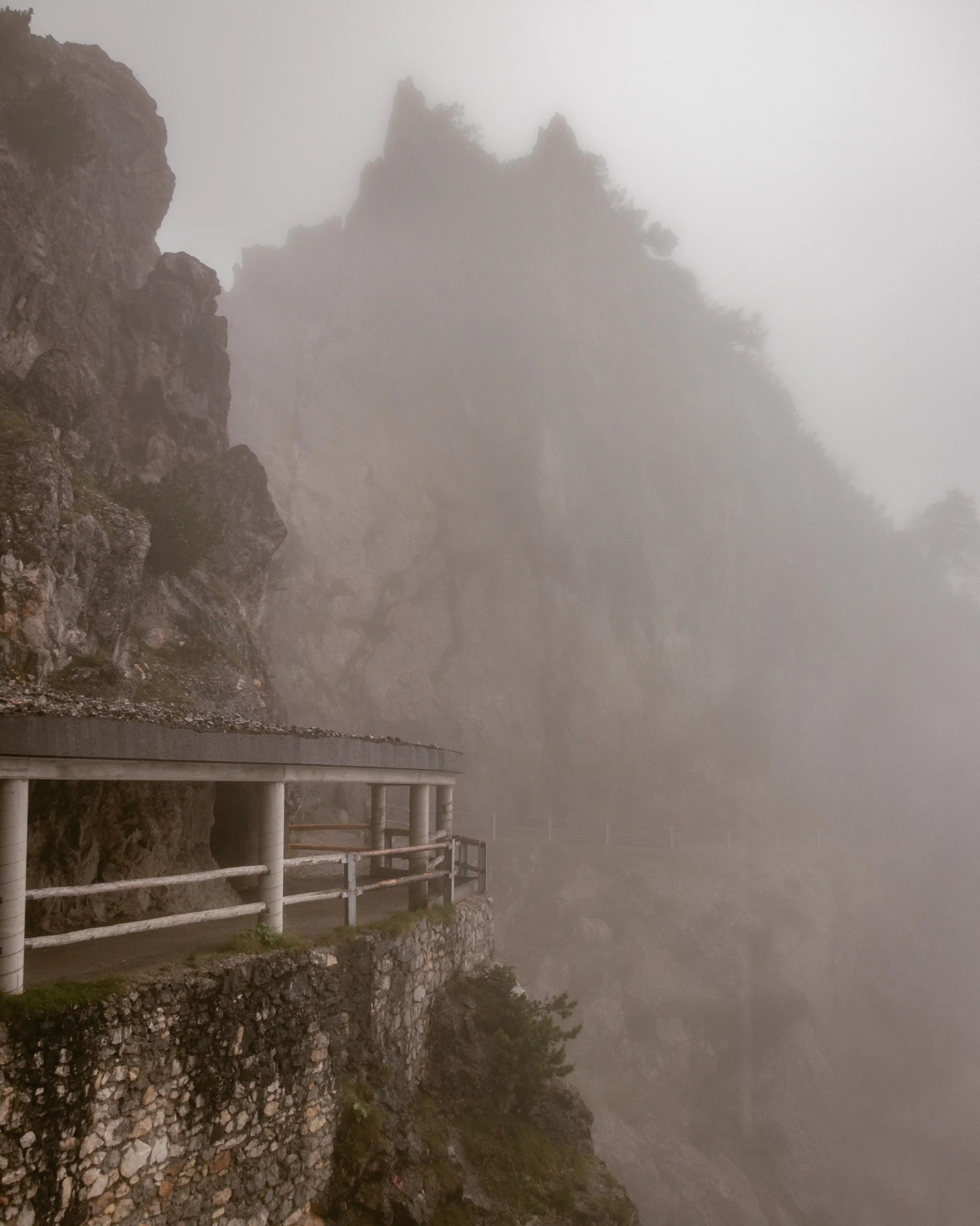 A narrow mountain walkway clings to a rocky cliff at Eisriesenwelt, partially disappearing into dense fog.