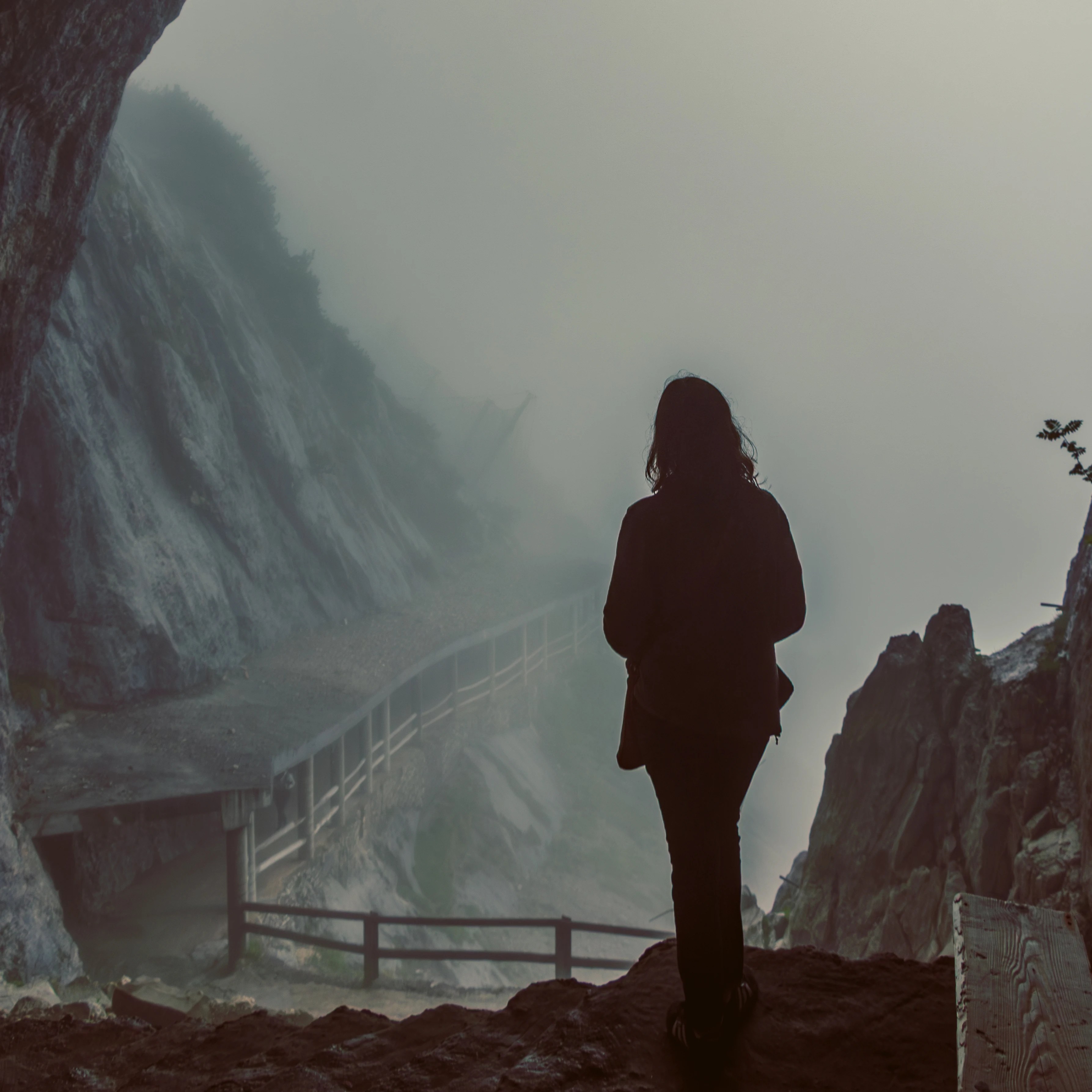 A person stands silhouetted at the entrance of a cave at Eisriesenwelt, looking out toward a fog-covered cliffside walkway.