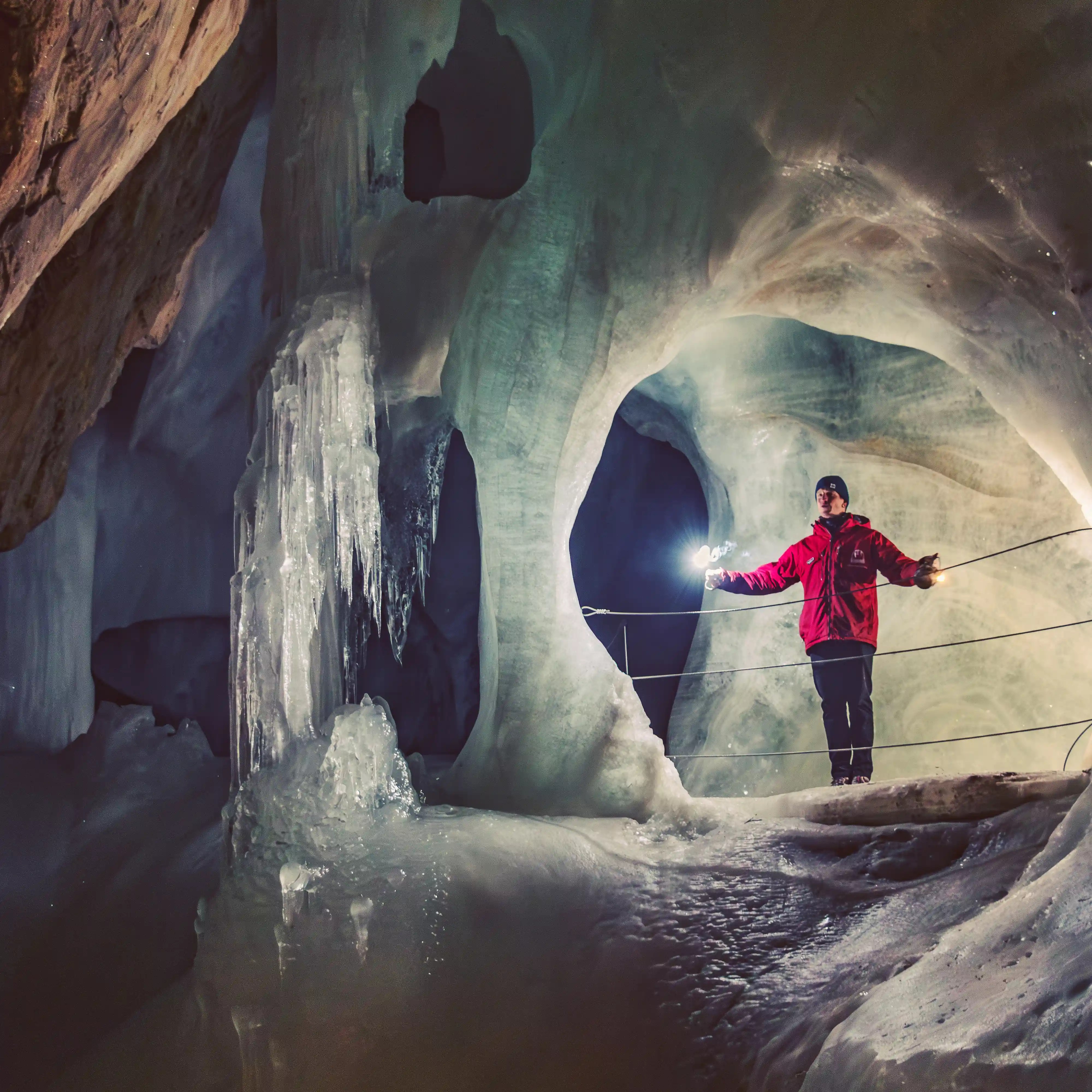 A guide in a red jacket stands beside massive ice formations inside Eisriesenwelt, holding a flare to illuminate the cave walls.
