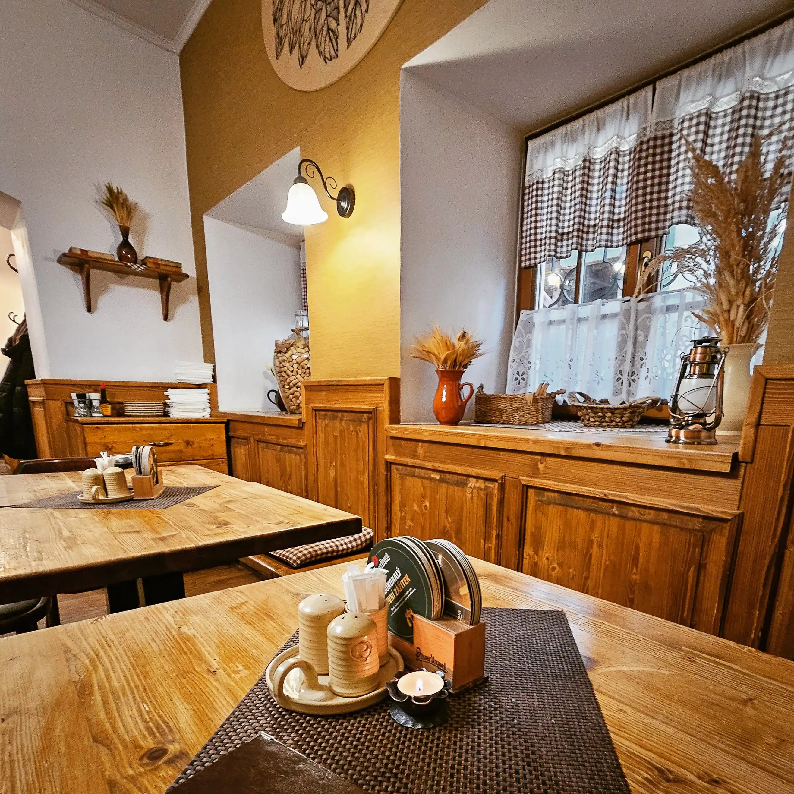 A warm wooden dining room with simple tables, checkered curtains, and traditional rustic decor in a Czech restaurant.