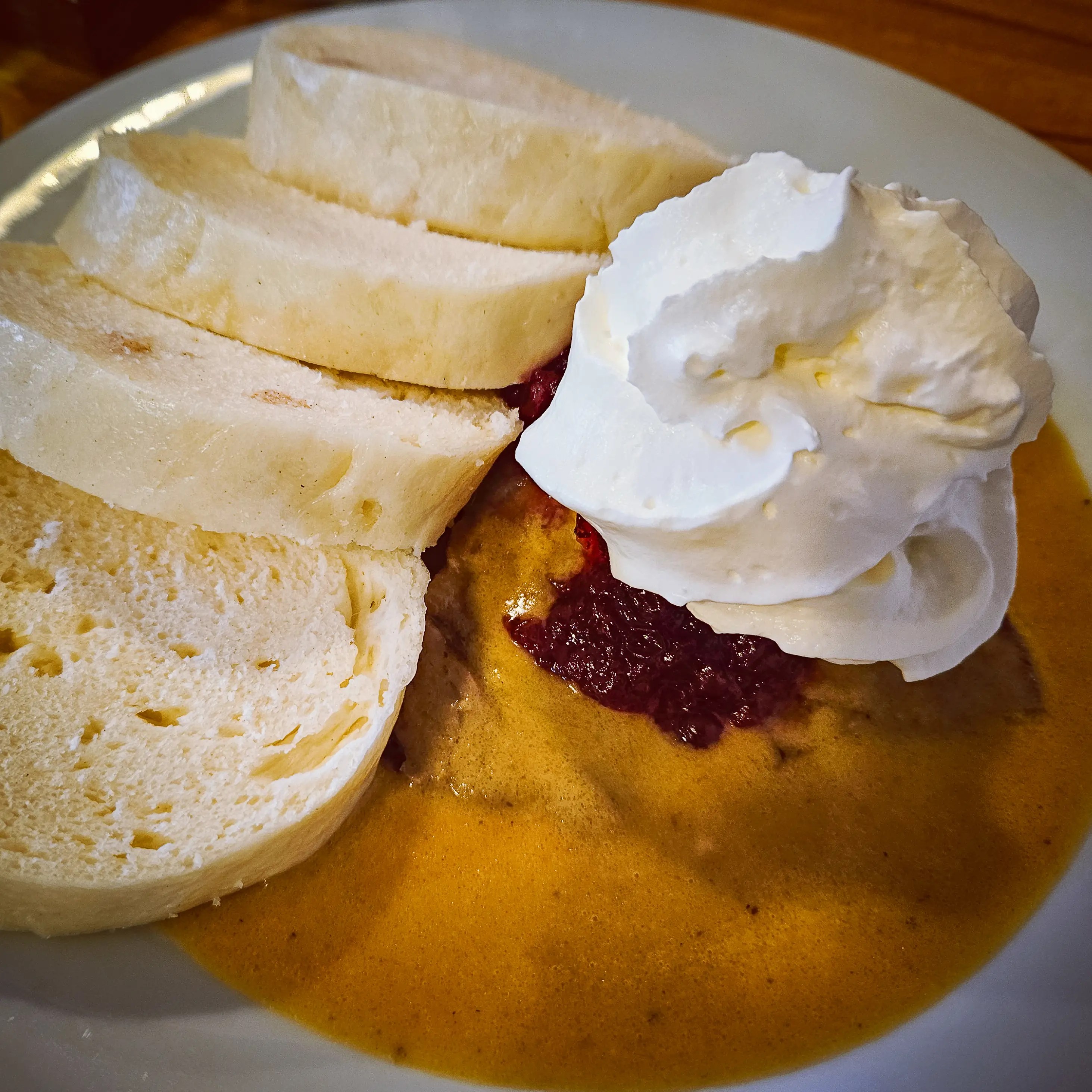 A plate of Czech-style roast meat in creamy sauce topped with lingonberry sauce and whipped cream, served with sliced bread dumplings.
