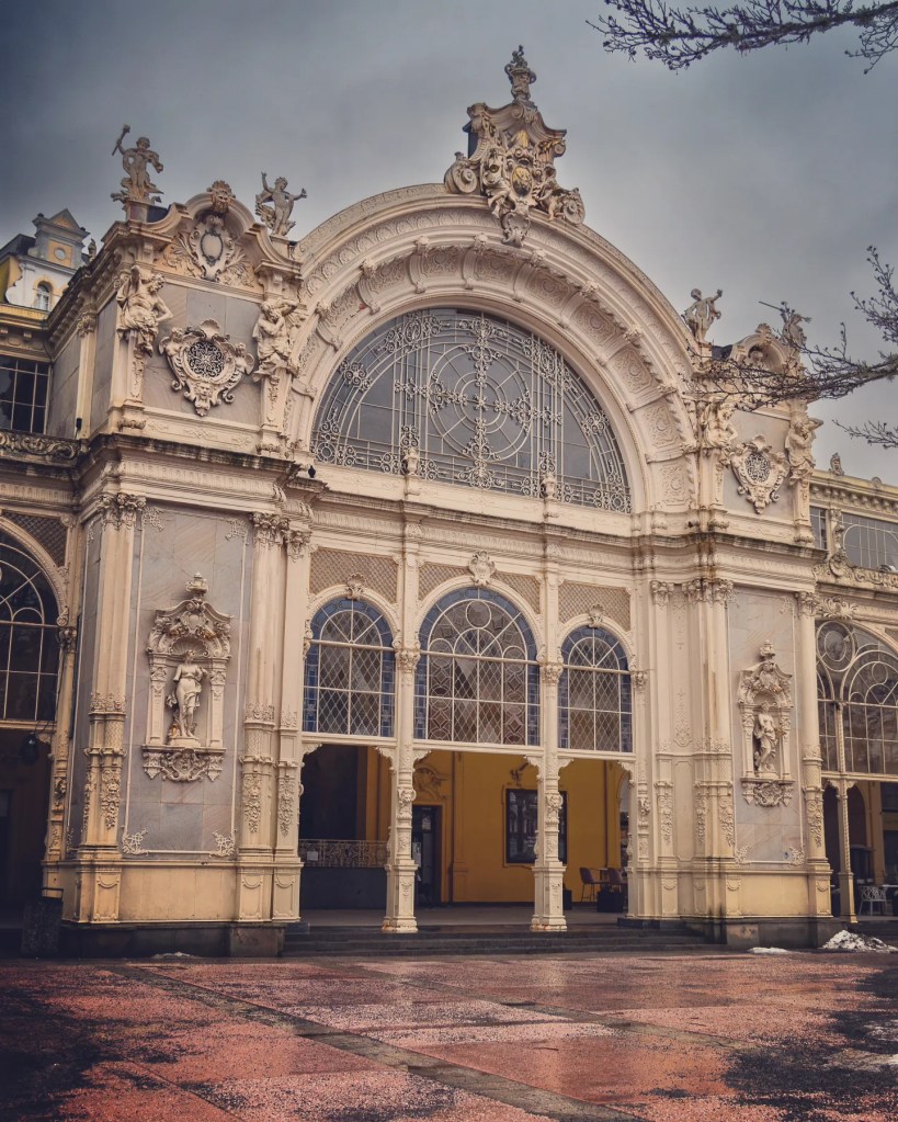 The ornate façade of the Main Colonnade with sculpted figures and a large arched window in Mariánské Lázně.