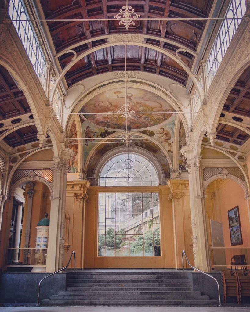 A staircase leading into the Main Colonnade beneath painted ceiling frescoes and carved arches.