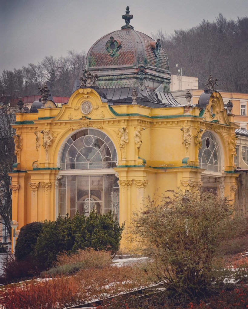 A yellow pavilion with statues and a green domed roof that forms part of the Main Colonnade complex in Mariánské Lázně.
