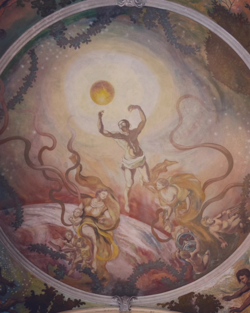 A ceiling fresco depicting allegorical figures surrounding a glowing sun inside the Main Colonnade.