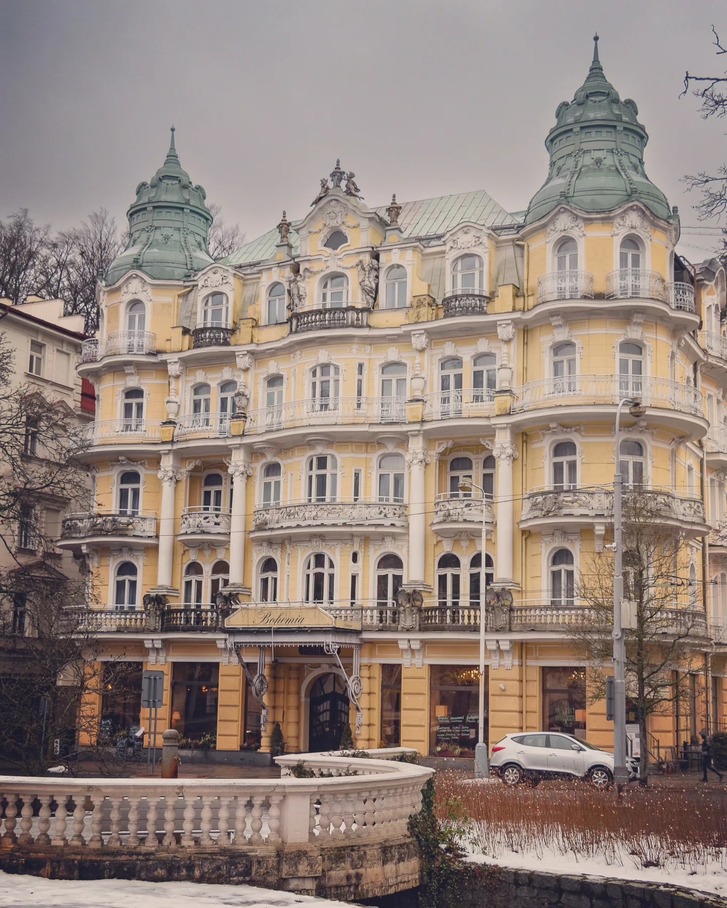 The ornate yellow façade of Hotel Bohemia with twin green domes and decorative balconies in Mariánské Lázně.