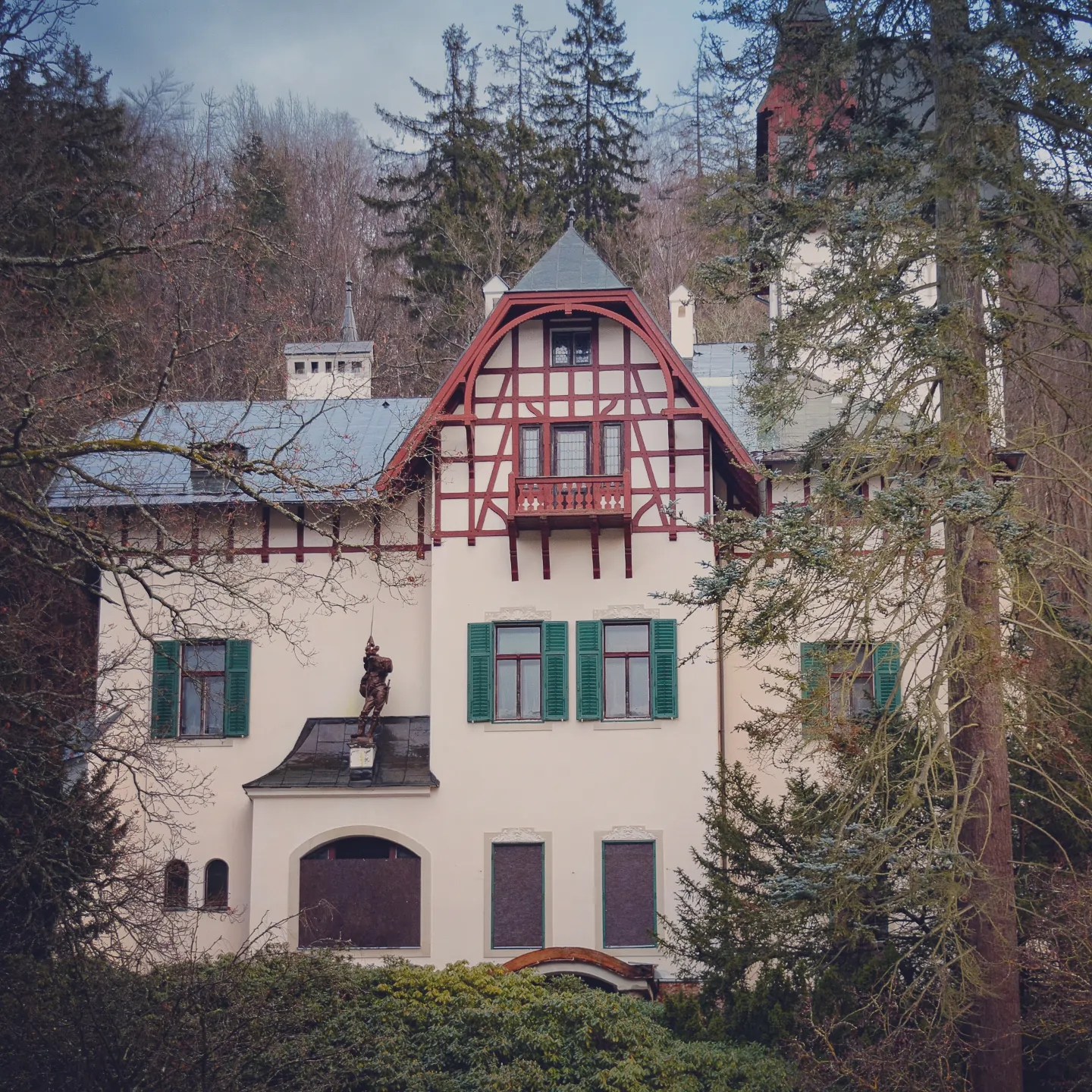 A cream-colored villa with red timber framing and green shutters surrounded by trees in Mariánské Lázně.